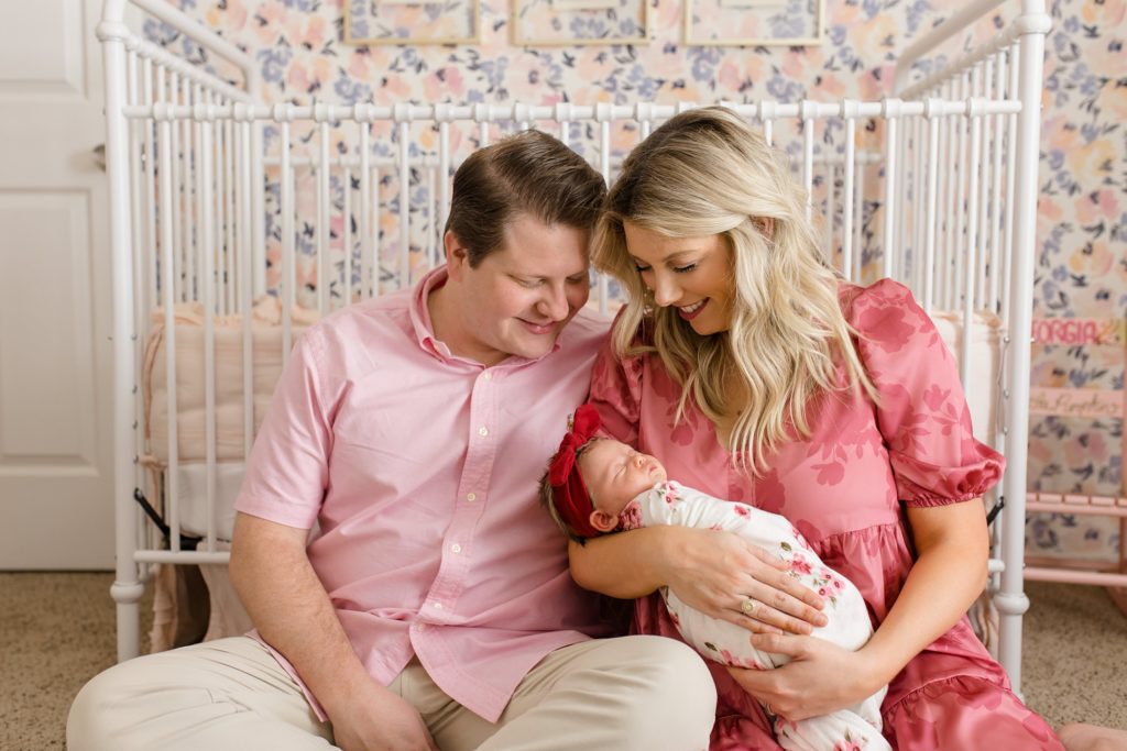 mom and dad hold baby girl by crib