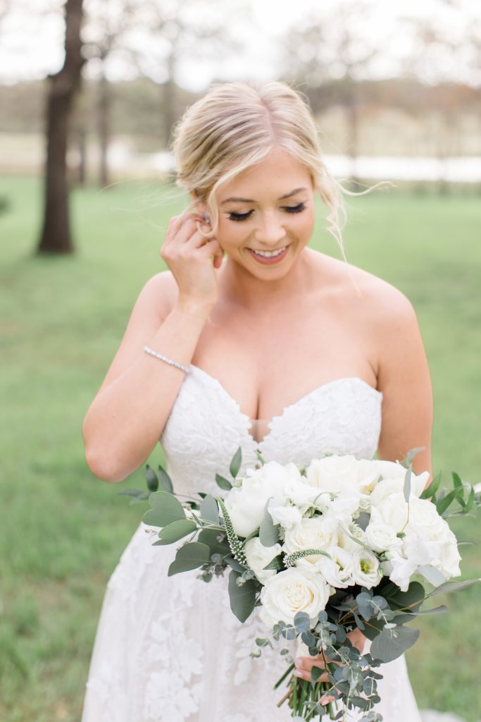 bride pushes hair behind her ear looking down at bouquet of white roses