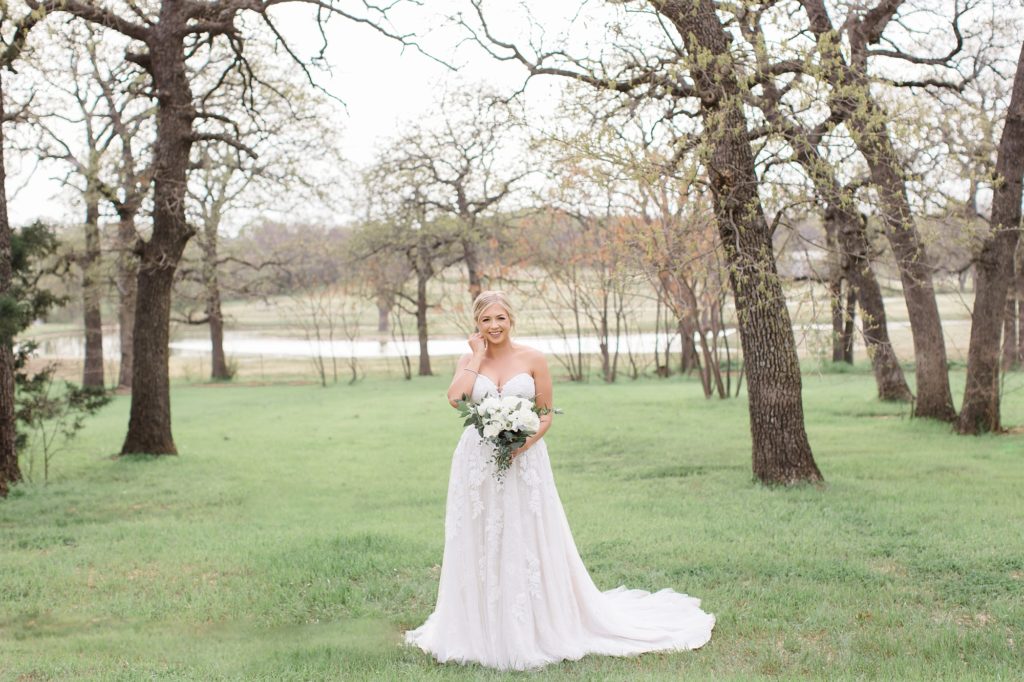 bride holds bouquet of all-white flowers in meadow at Oak + Ivy