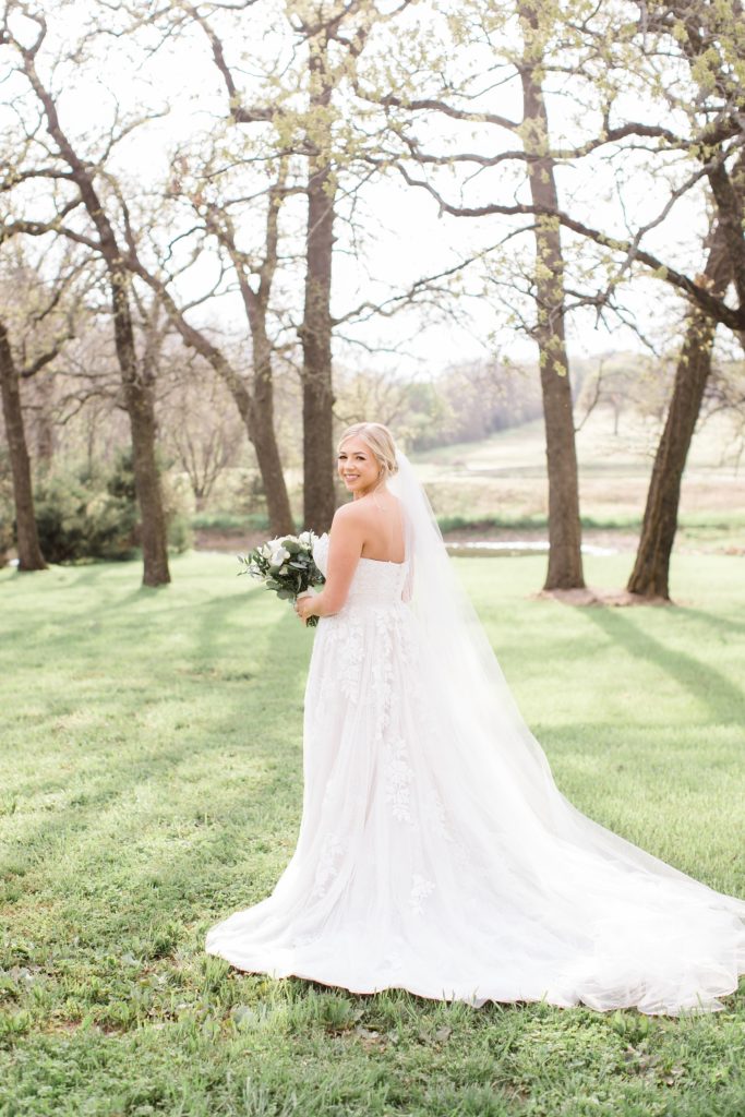 bride holds bouquet with white flowers in meadow at Oak + Ivy