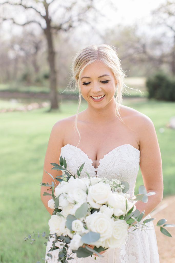 bride looks down at bouquet of white roses