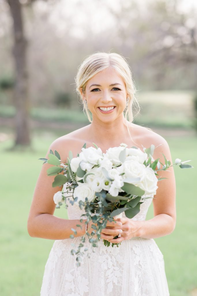 bride holds bouquet of white roses smiling during bridal portraits 