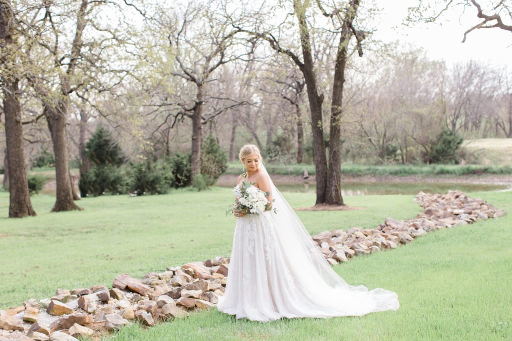 bride poses near creek with stones at Oak + Ivy