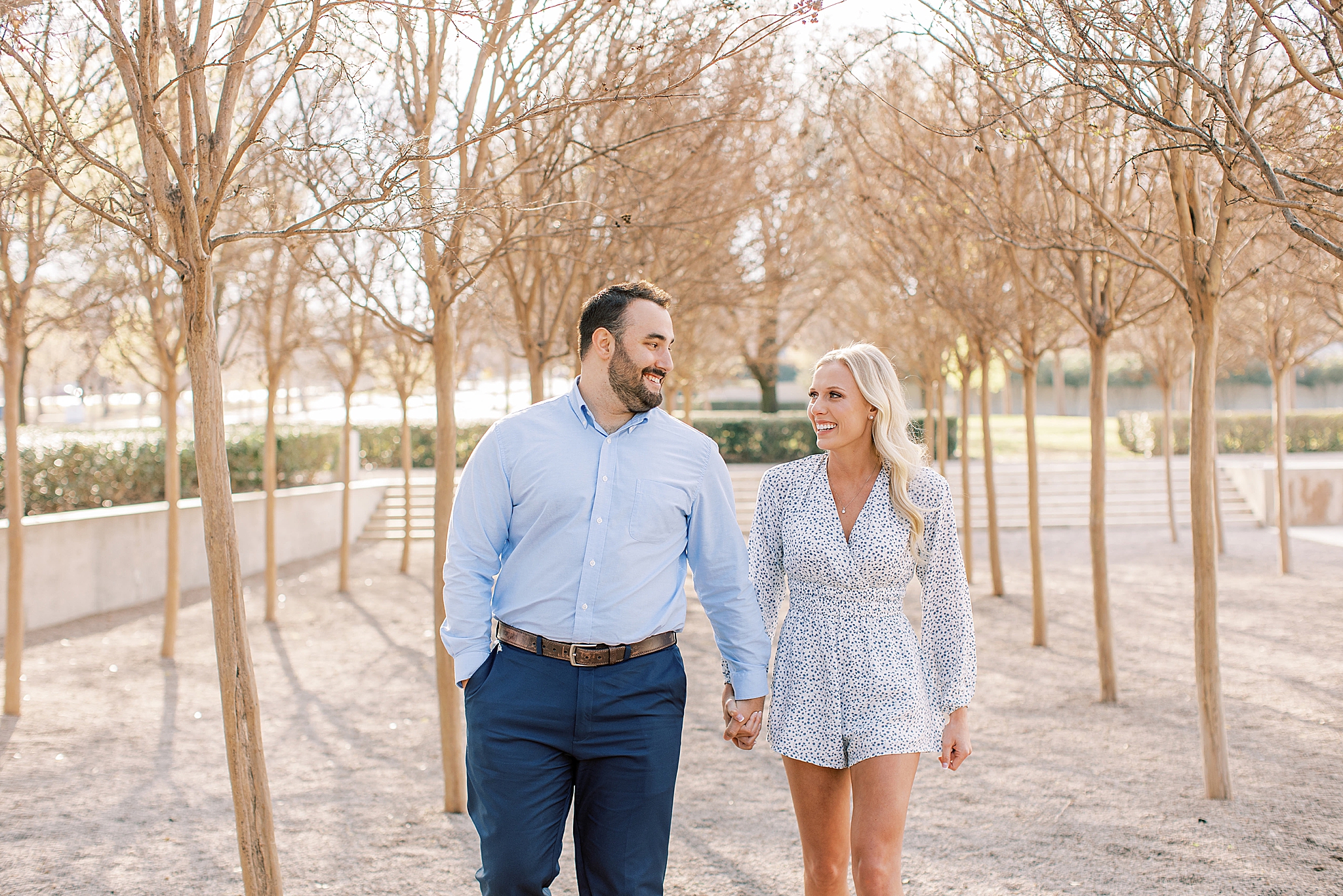 engaged couple walks through grove of trees at Kimball Art Museum