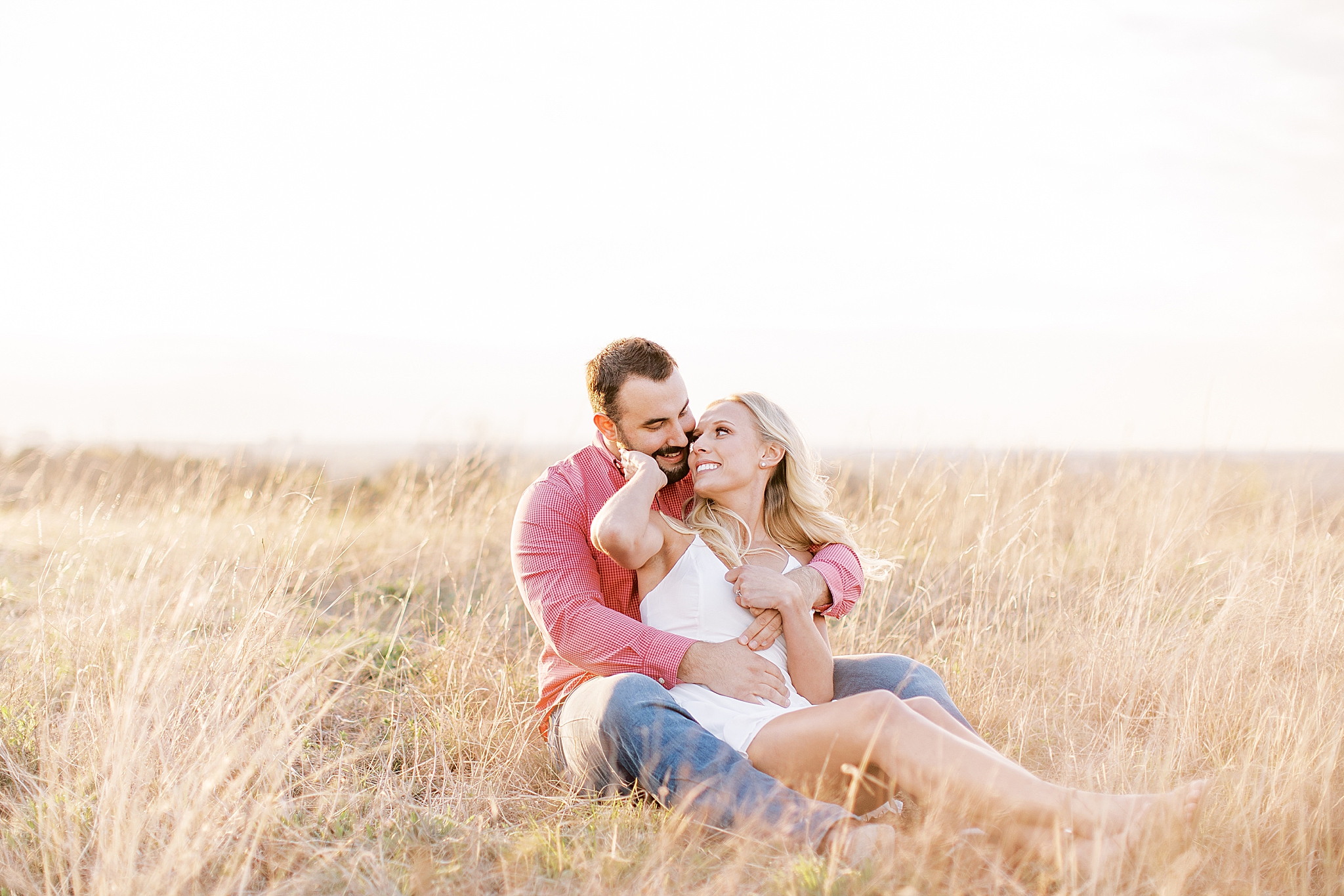 bride and groom sit in field during Tandy Hills engagement session
