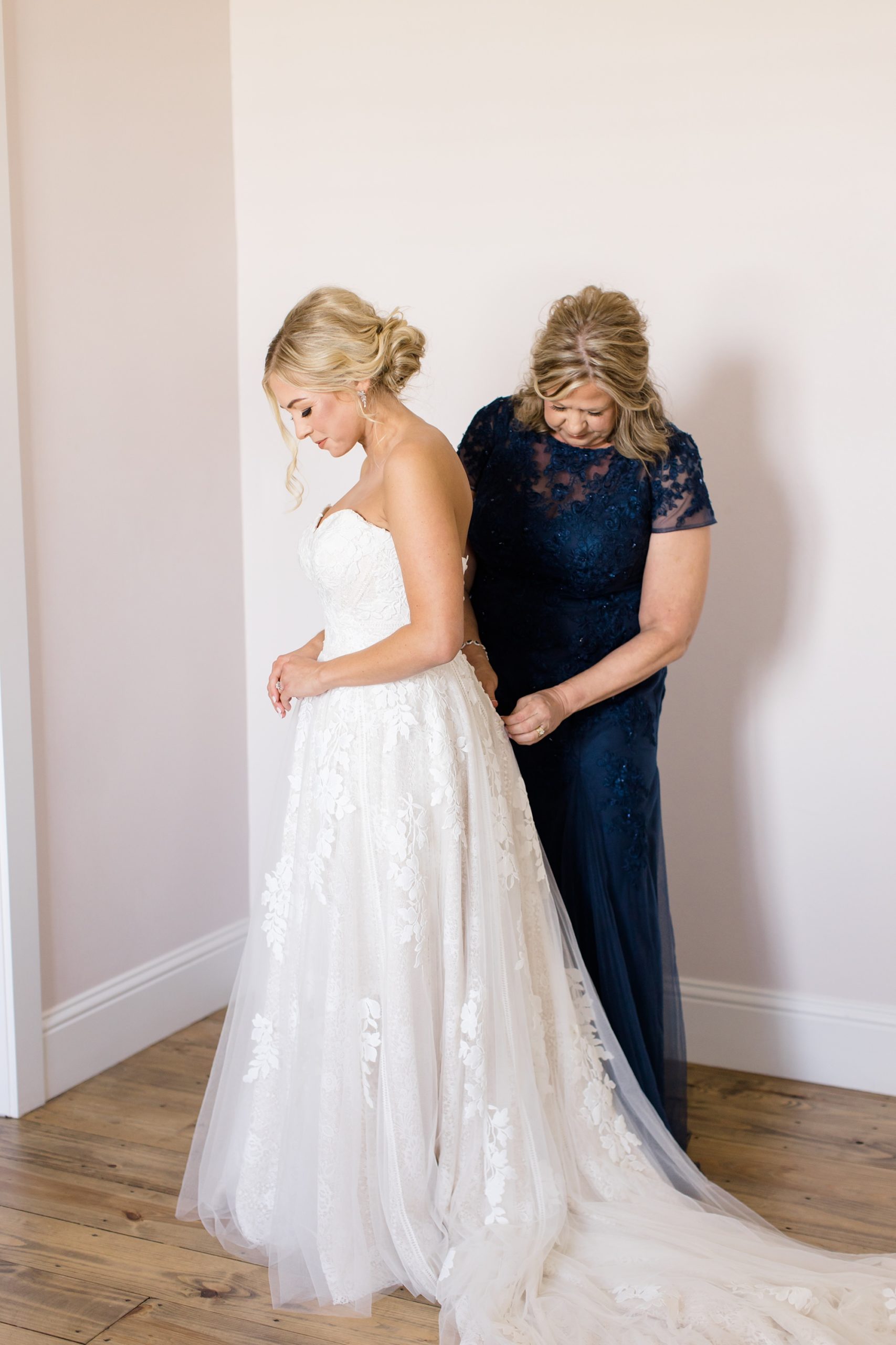 mother of bride helps her into wedding dress