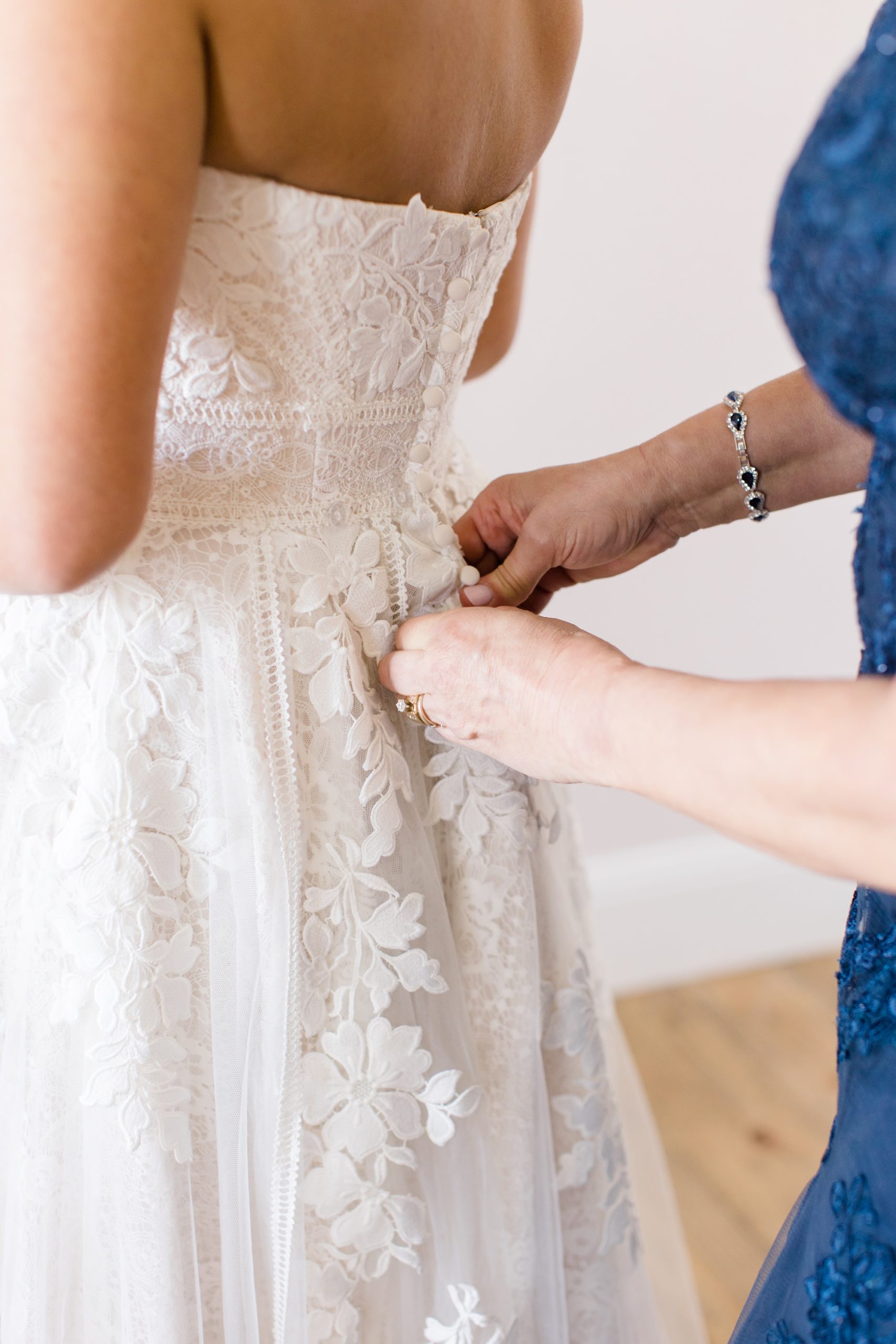 mother helps bride with wedding dress buttons