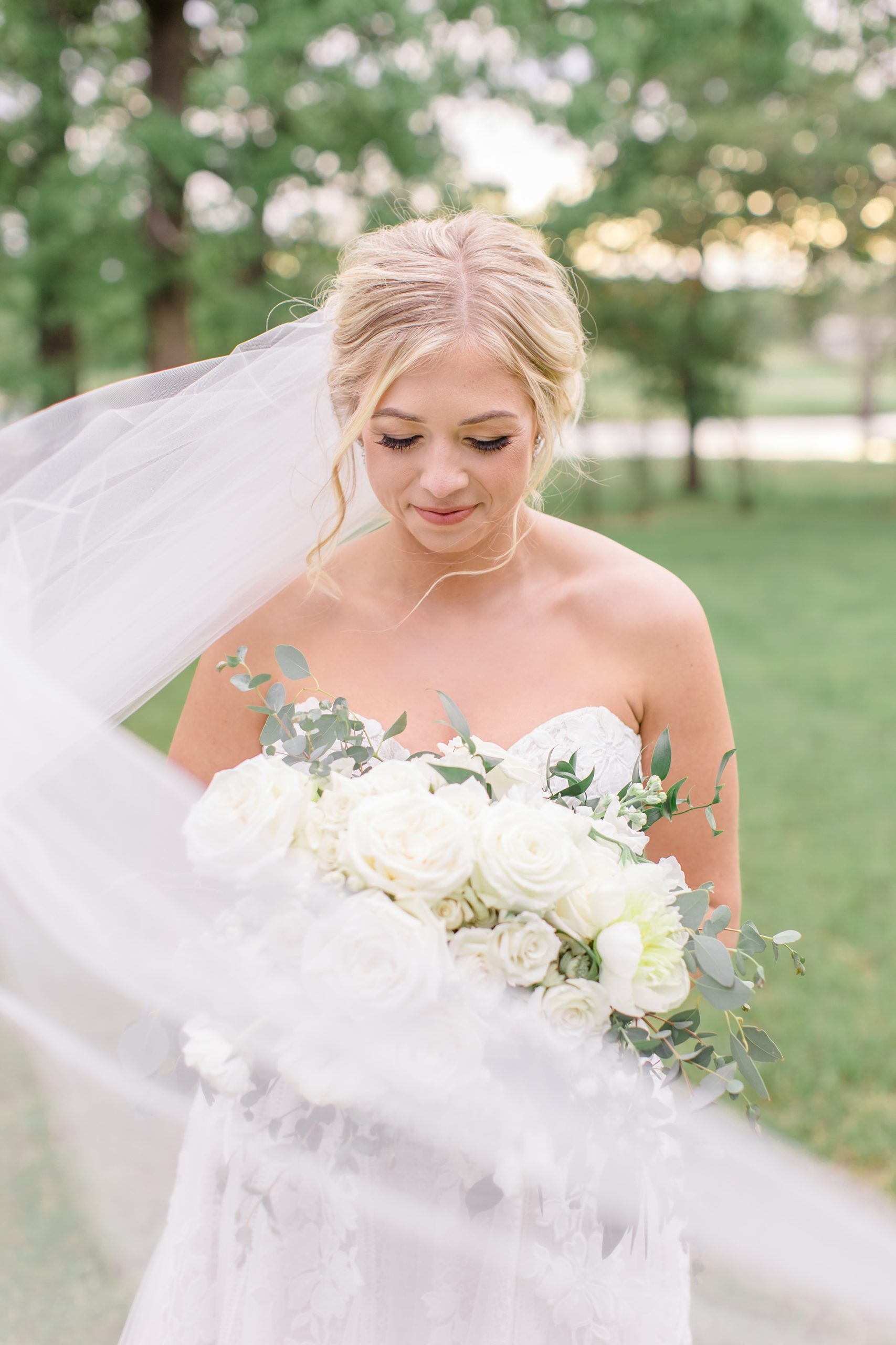 bride looks down at bouquet with veil wrapped around shoulder 