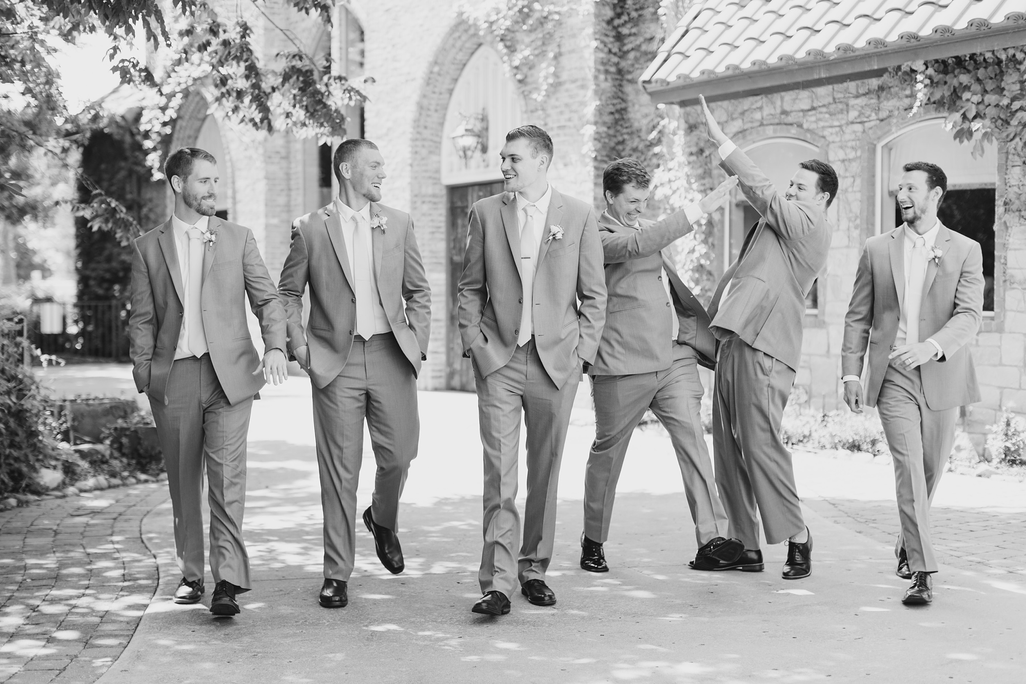 groom laughs while groomsmen high five outside Aristide Mansfield