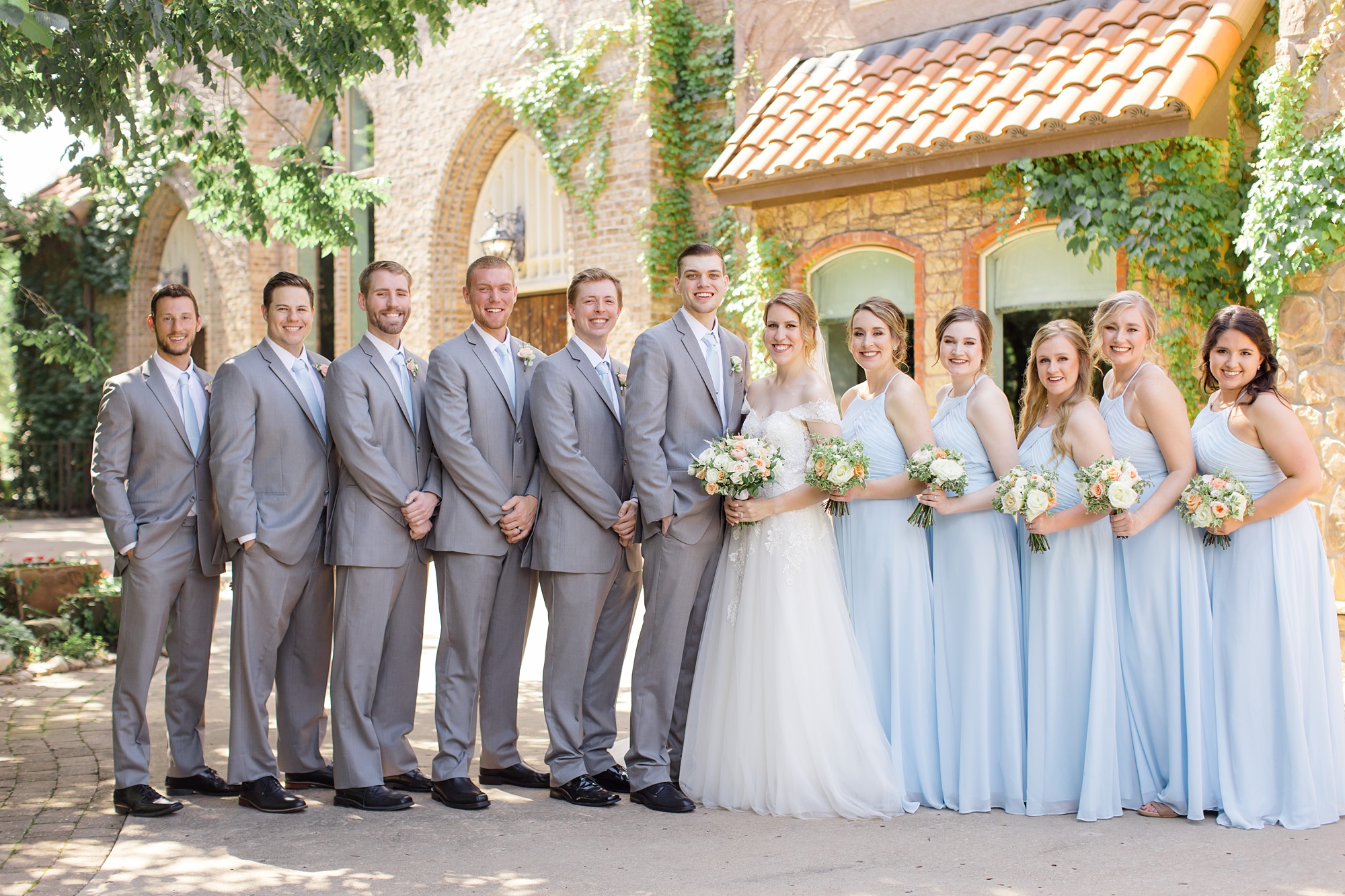 bride and groom pose with wedding party in light blue dresses and grey suits