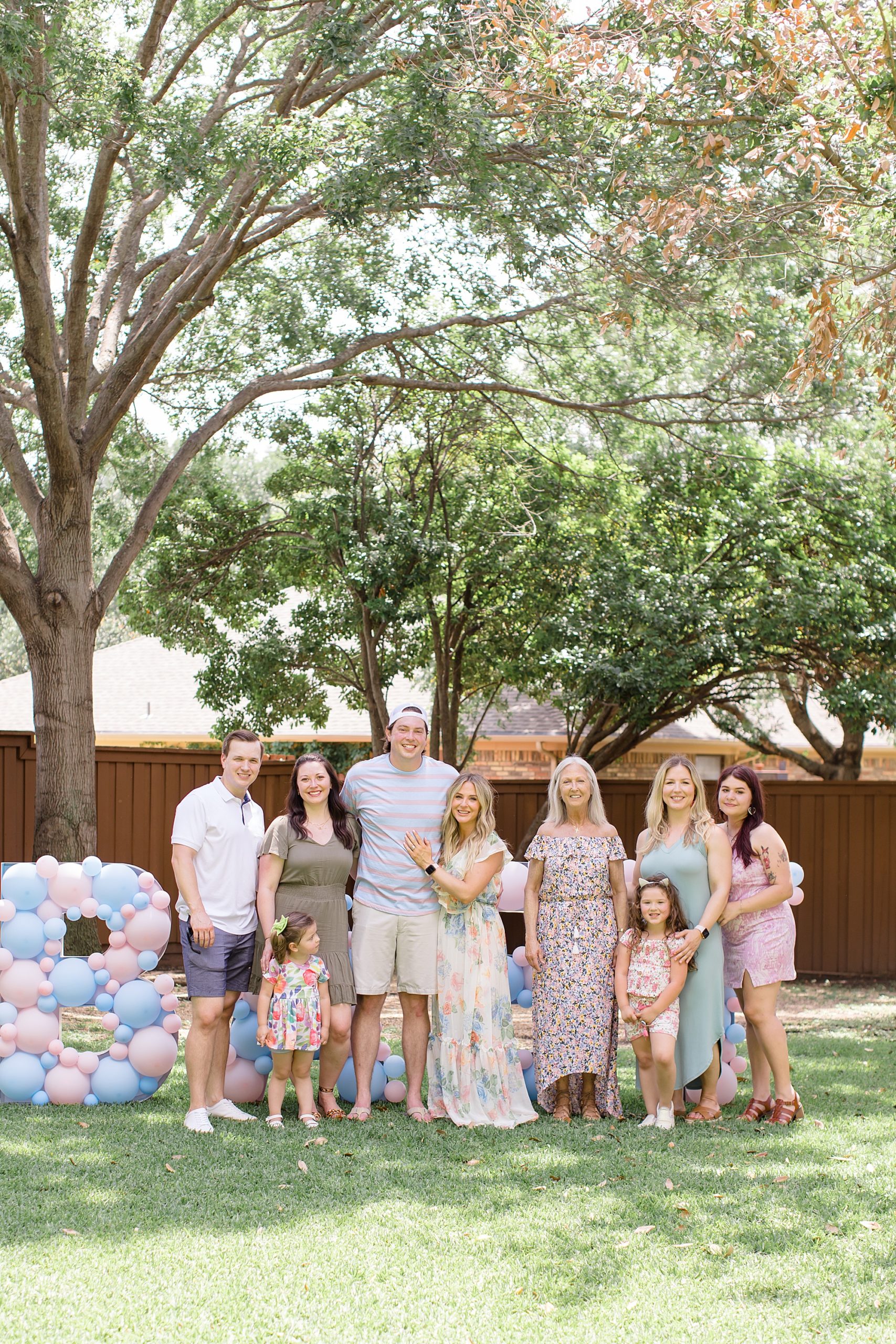 expecting parents pose with family by BABY sign in backyard