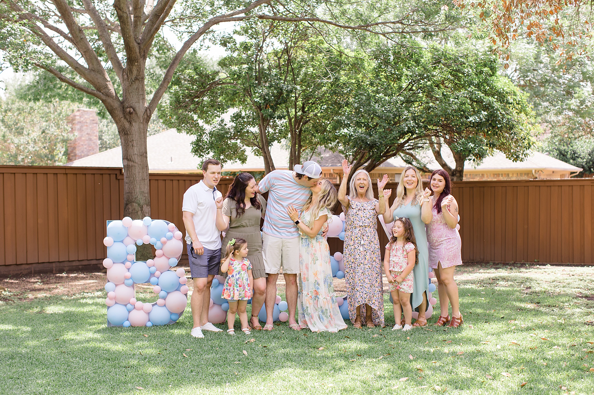 couple kisses with family surrounding them during gender reveal party