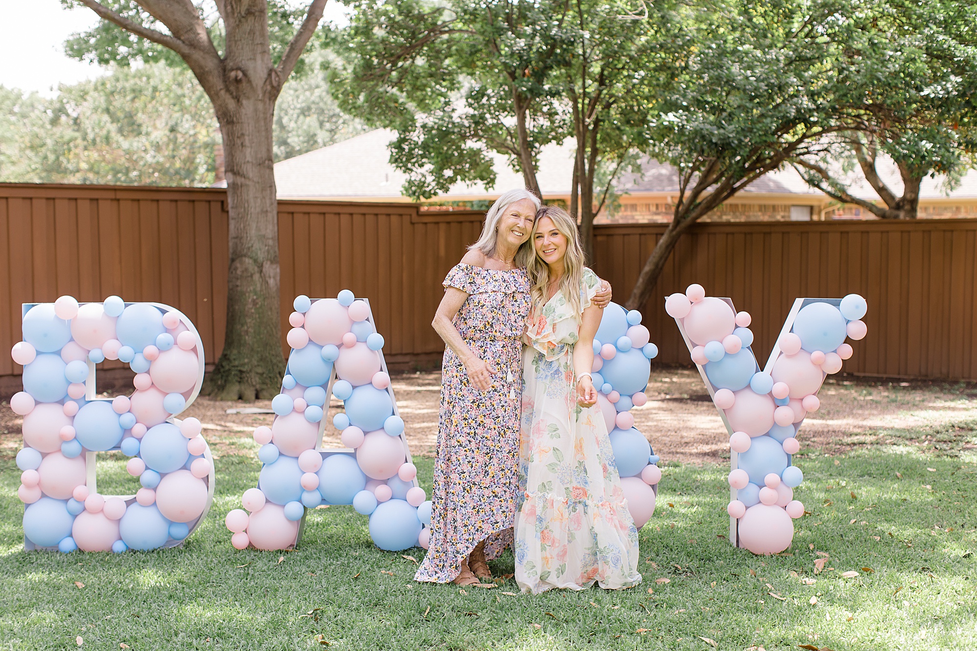 mom and daughter pose by BABY sign in backyard