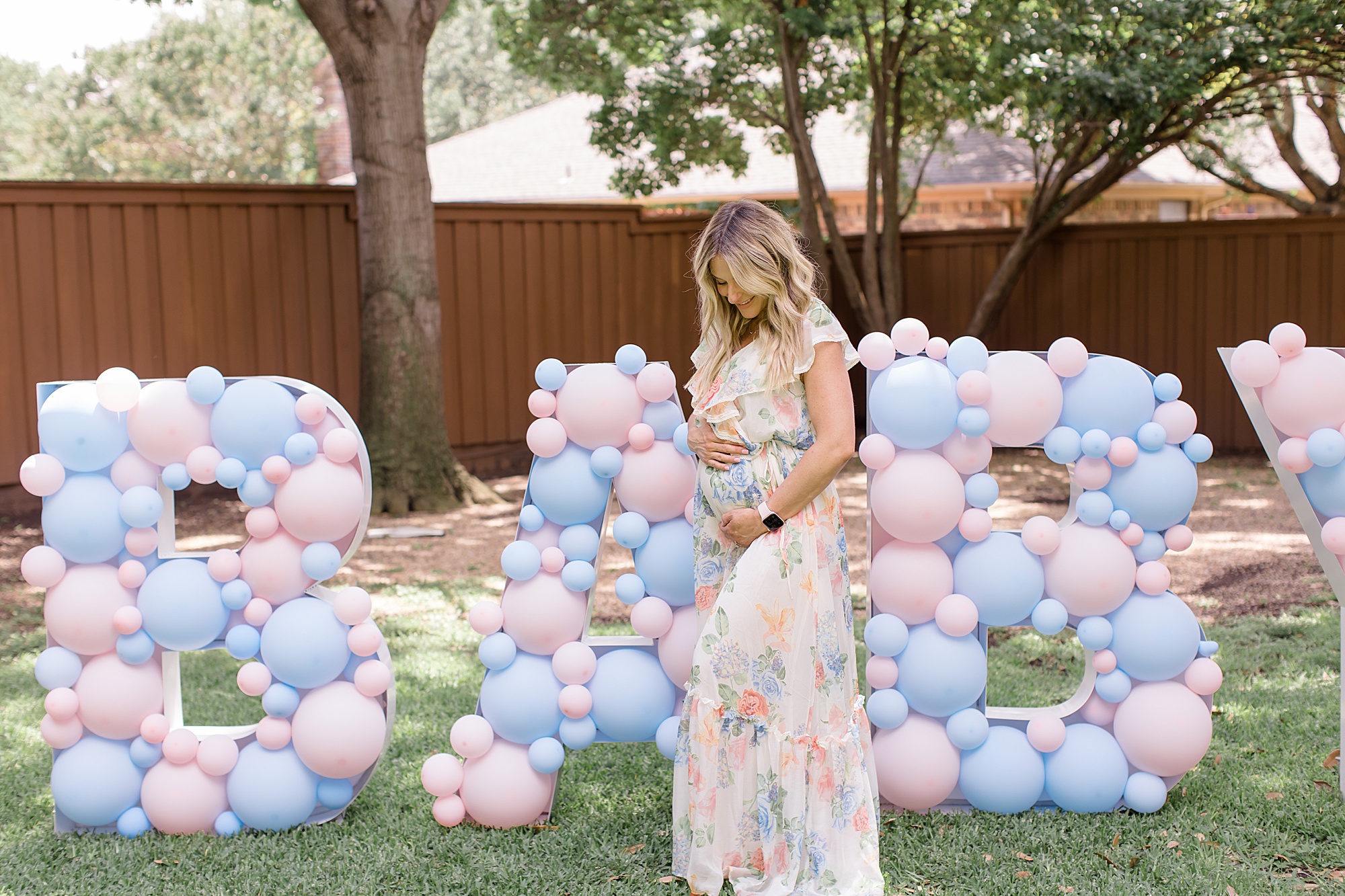 expecting mom holds belly in backyard during gender reveal party