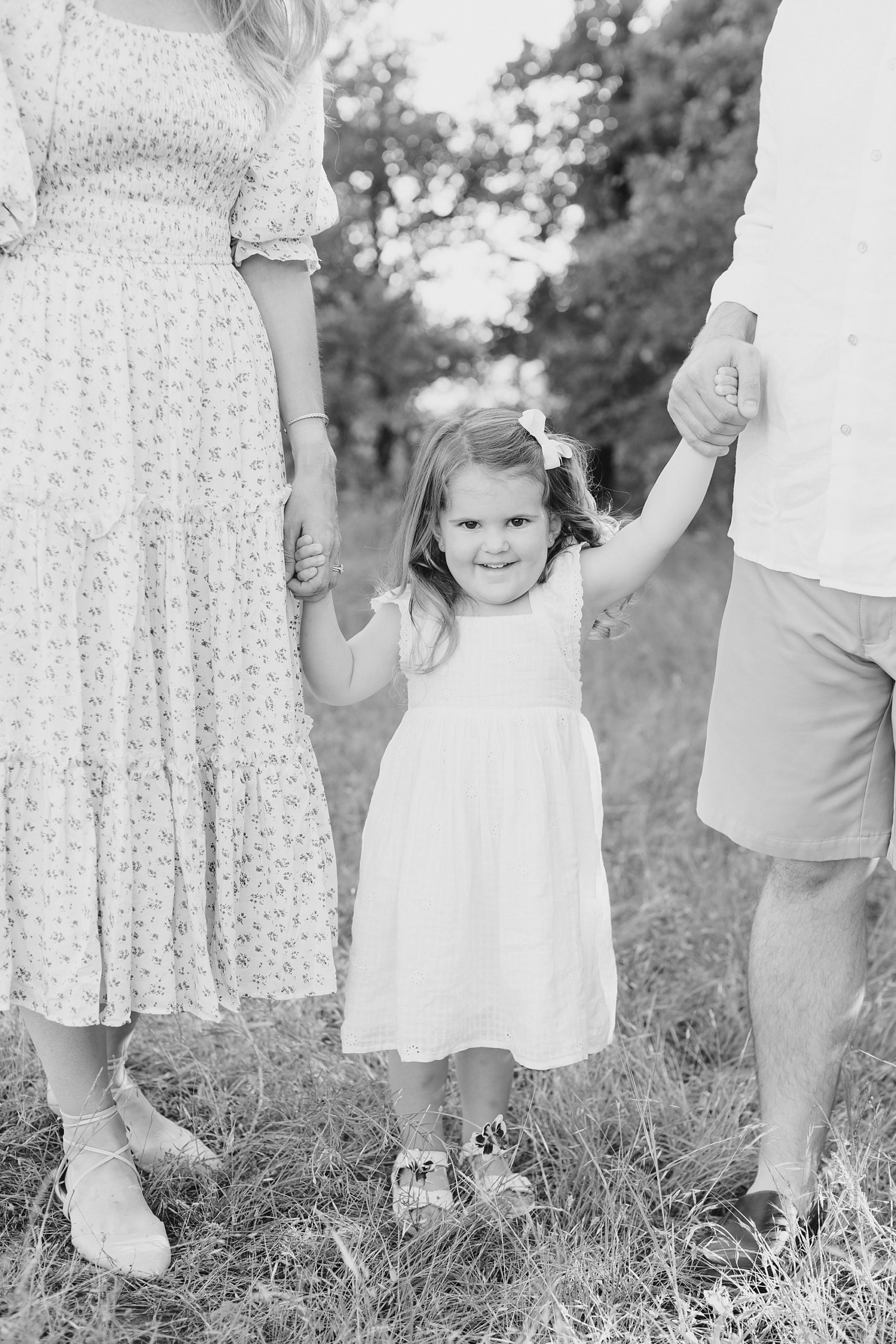 parents hold toddler's hand during spring family portraits at Murrell Park