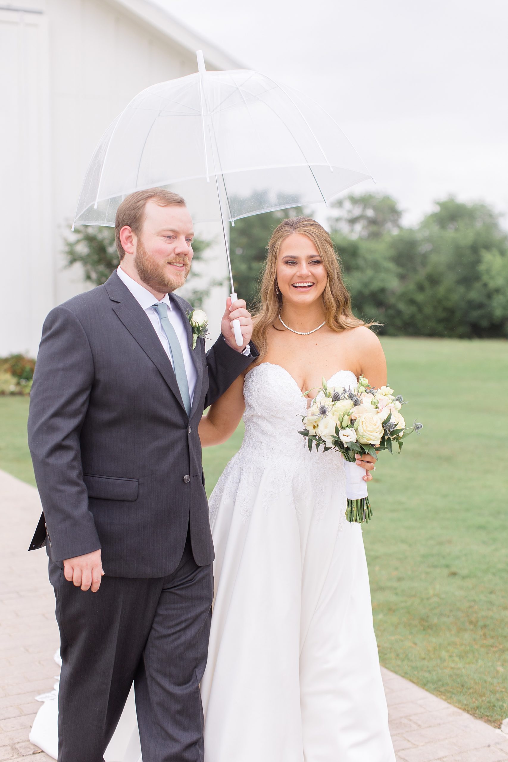 bride and groom walk under clear umbrella on rainy wedding day in Texas