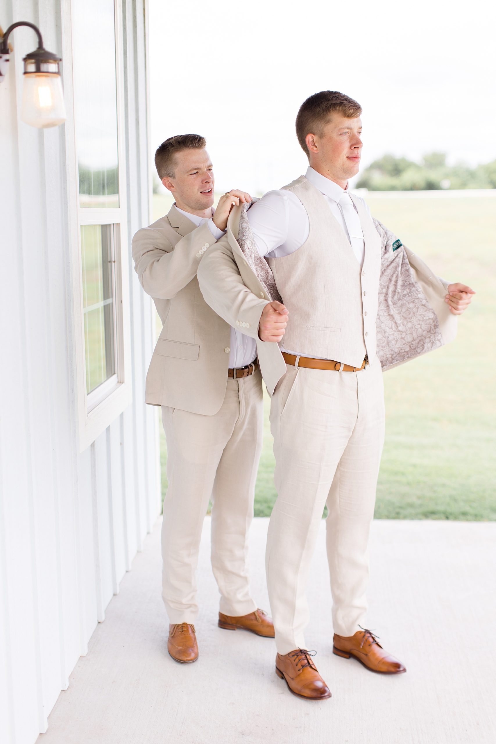 groomsman helps groom with tan suit for TX wedding