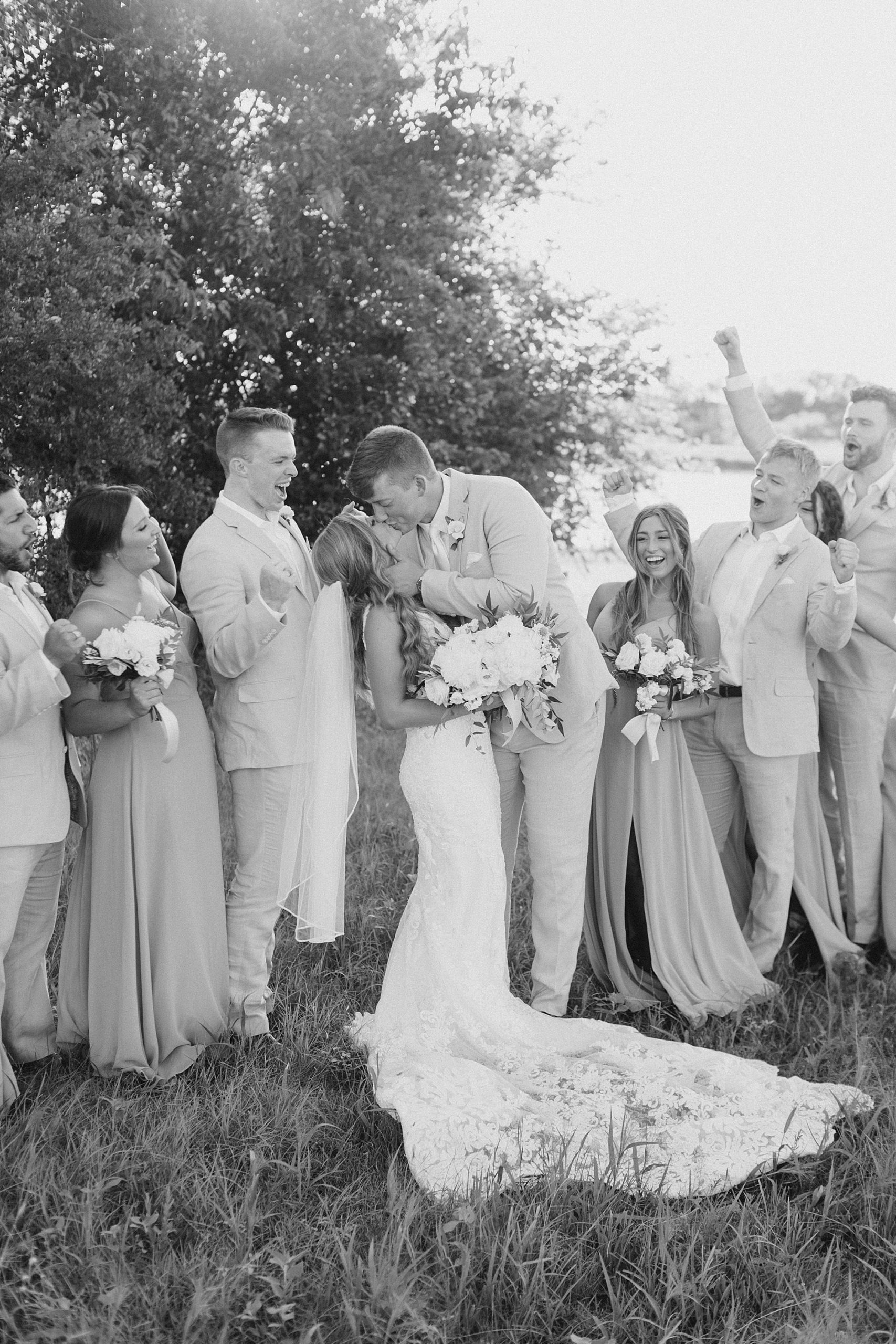 bride and groom kiss with wedding party cheering them on