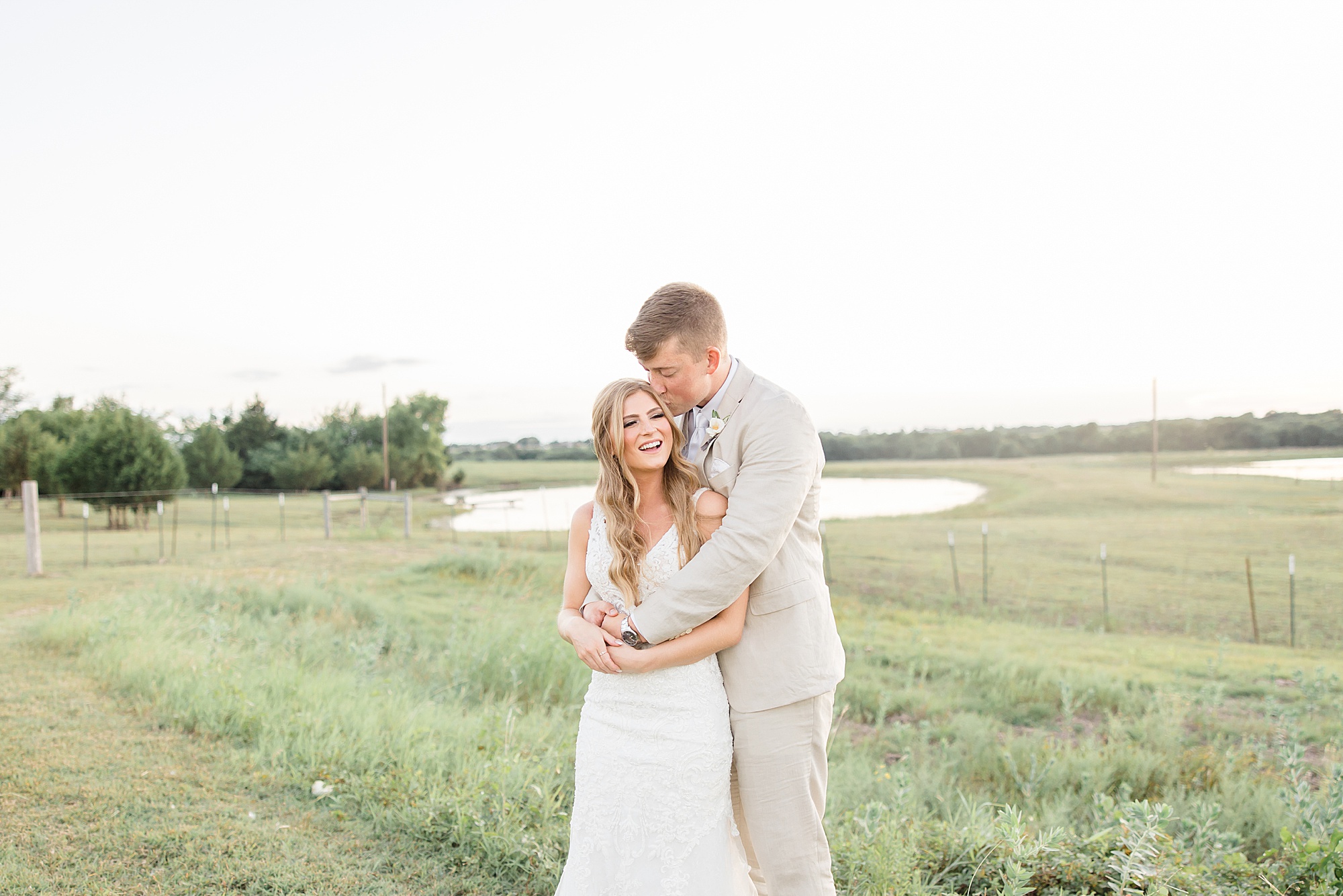 bride and groom hug in field at sunset