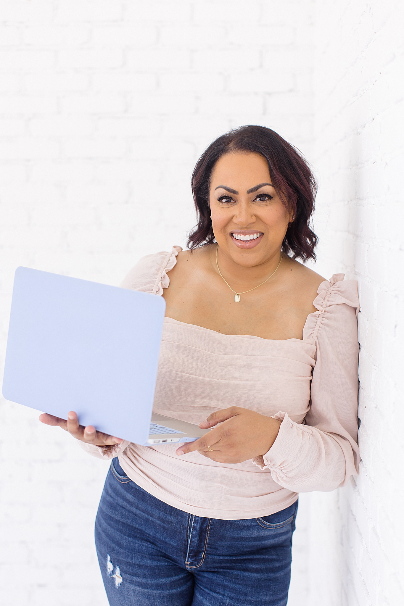 woman holds laptop leaning against white wall