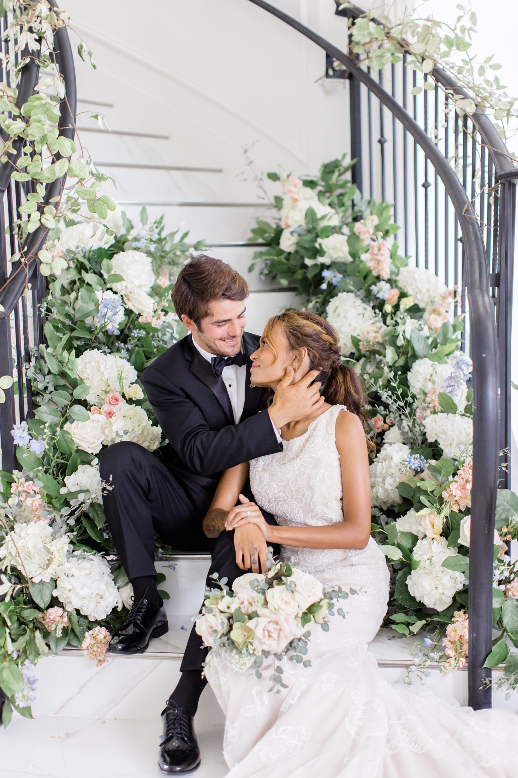 newlyweds sit on staircase draped with flowers at The Hillside Estate