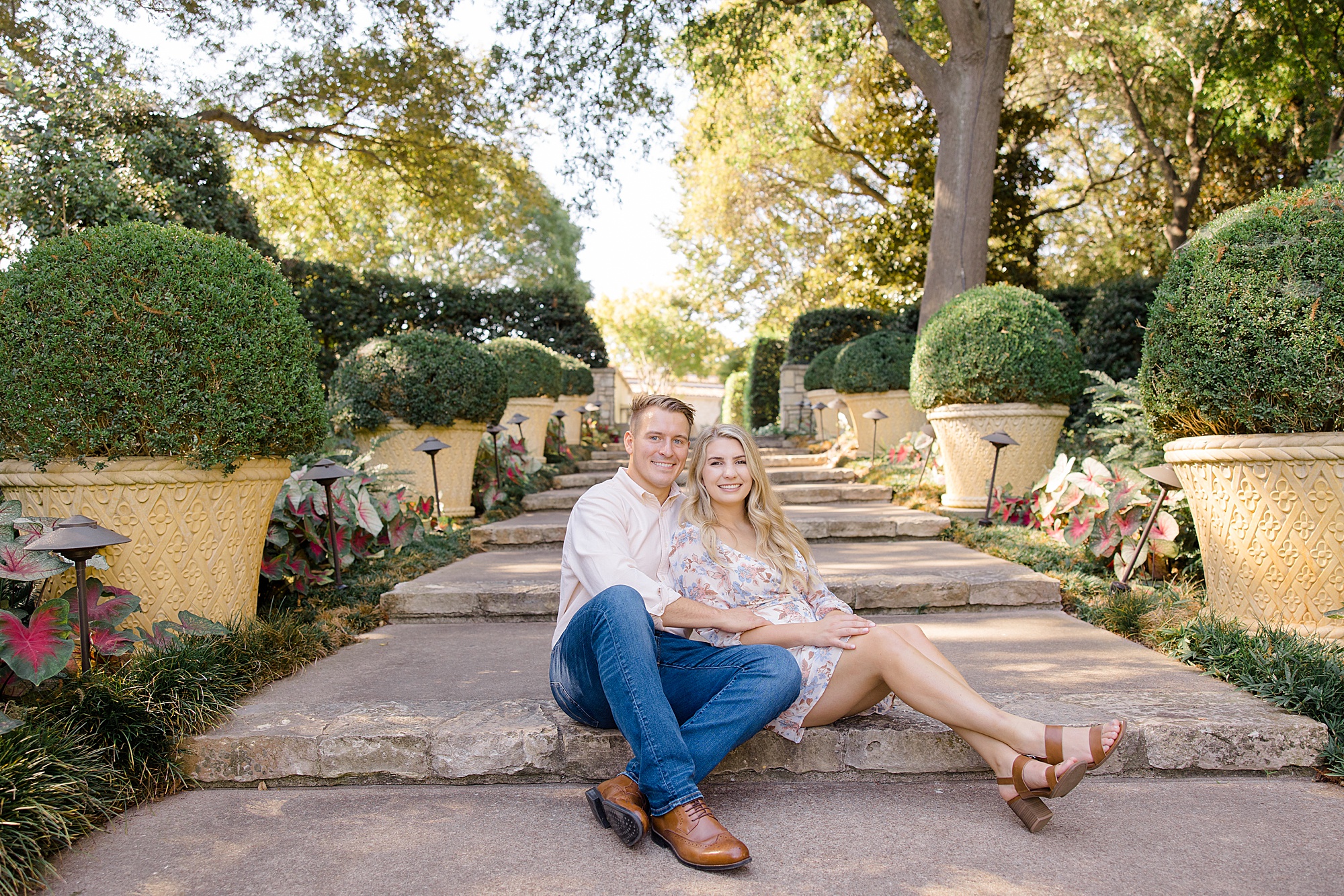 engaged couple sits on steps at Dallas Arboretum
