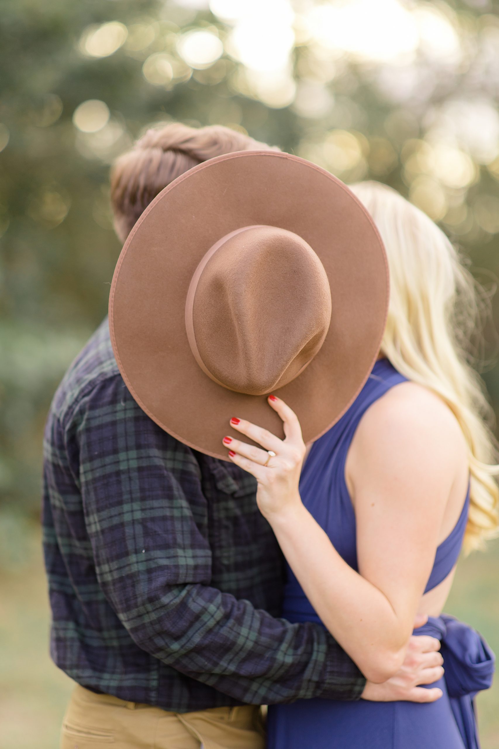 engaged couple kisses behind wide brimmed hat during Rockledge Park engagement session