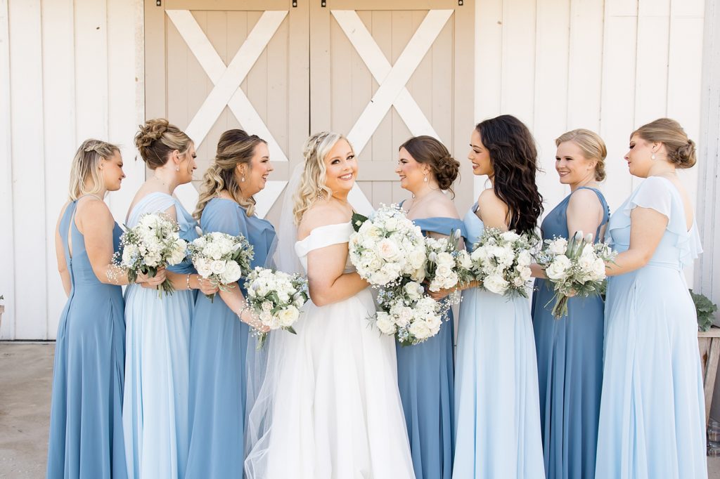 bride holds bouquet and looks over her shoulder during photos iwht bridesmaids in light blue gowns