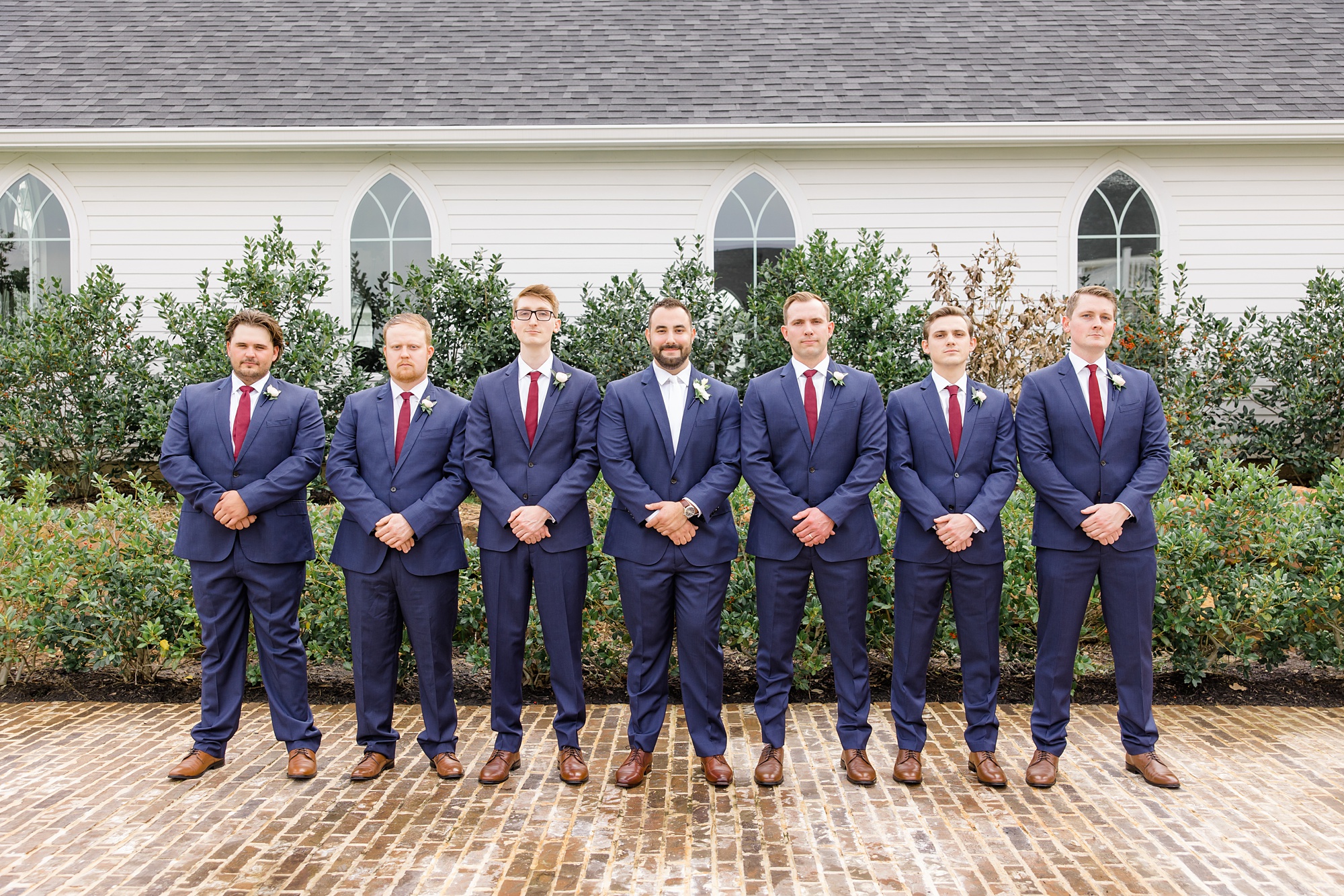 groomsmen stand with groom in navy suits with red ties