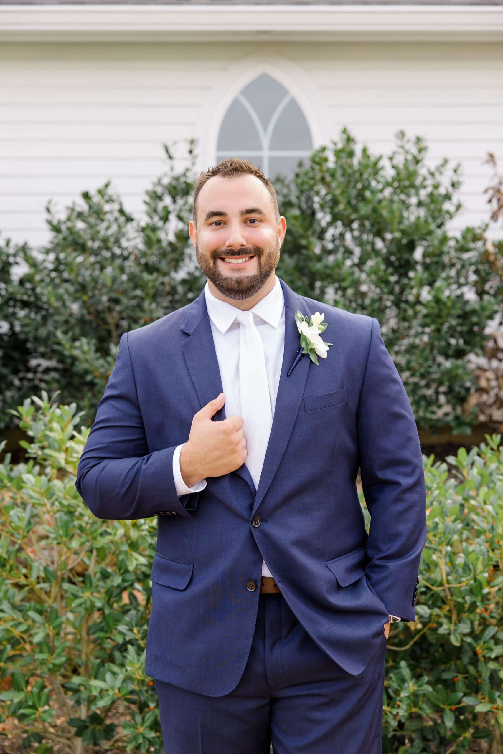 groom stands in navy suit with ivory tie