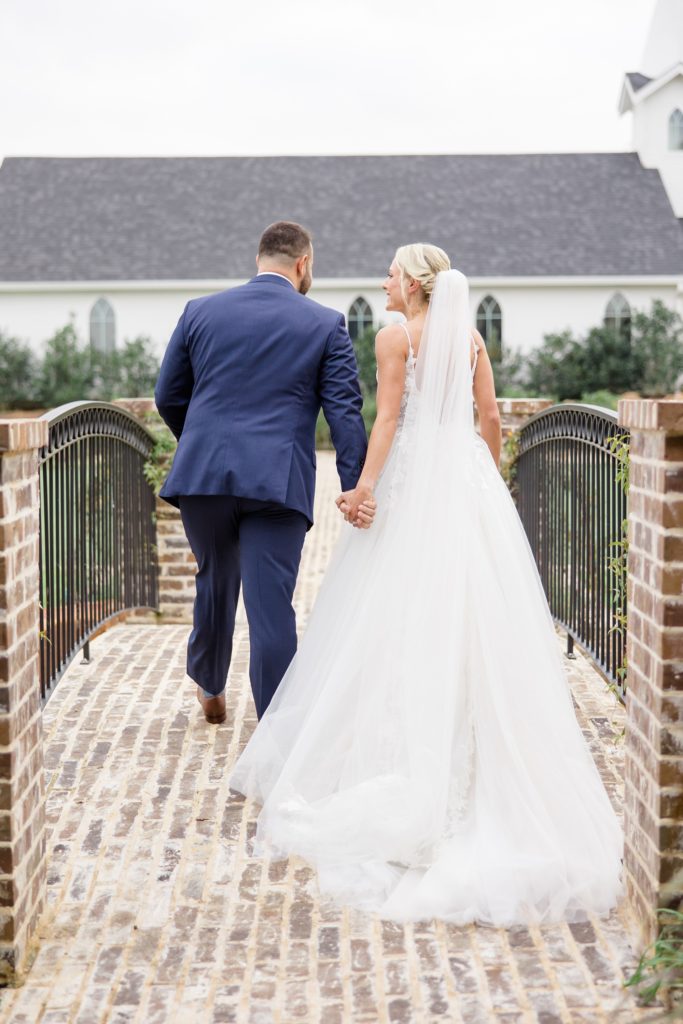 bride and groom walk over brick bridge at The Springs at Valley View
