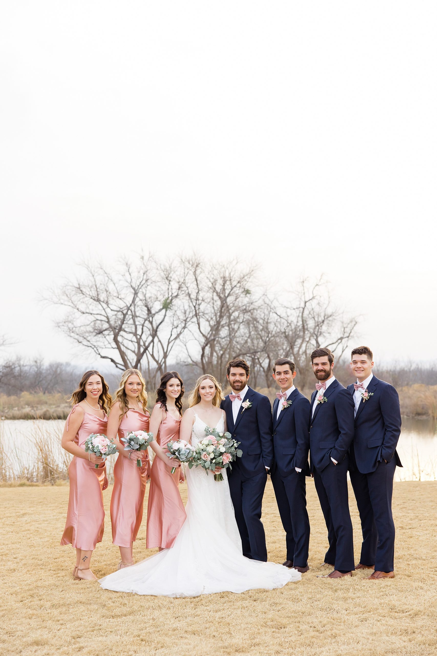 bride and groom stand with wedding party in pink and blue