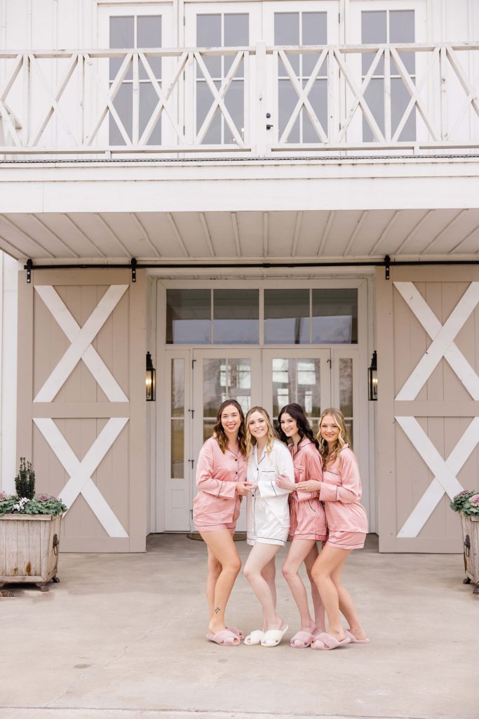 bridesmaids in matching pink robes pose outside The Nest at Ruth Farms