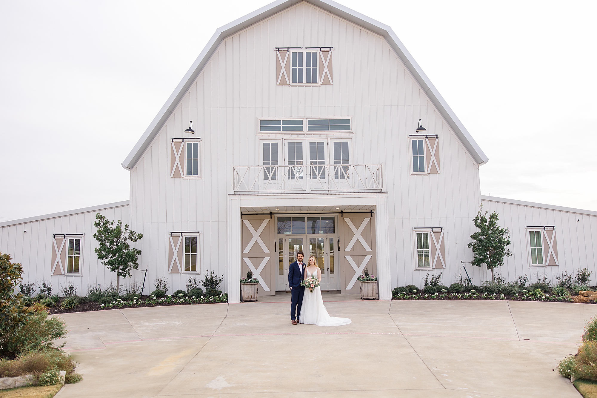 bride and groom stand outside white barn