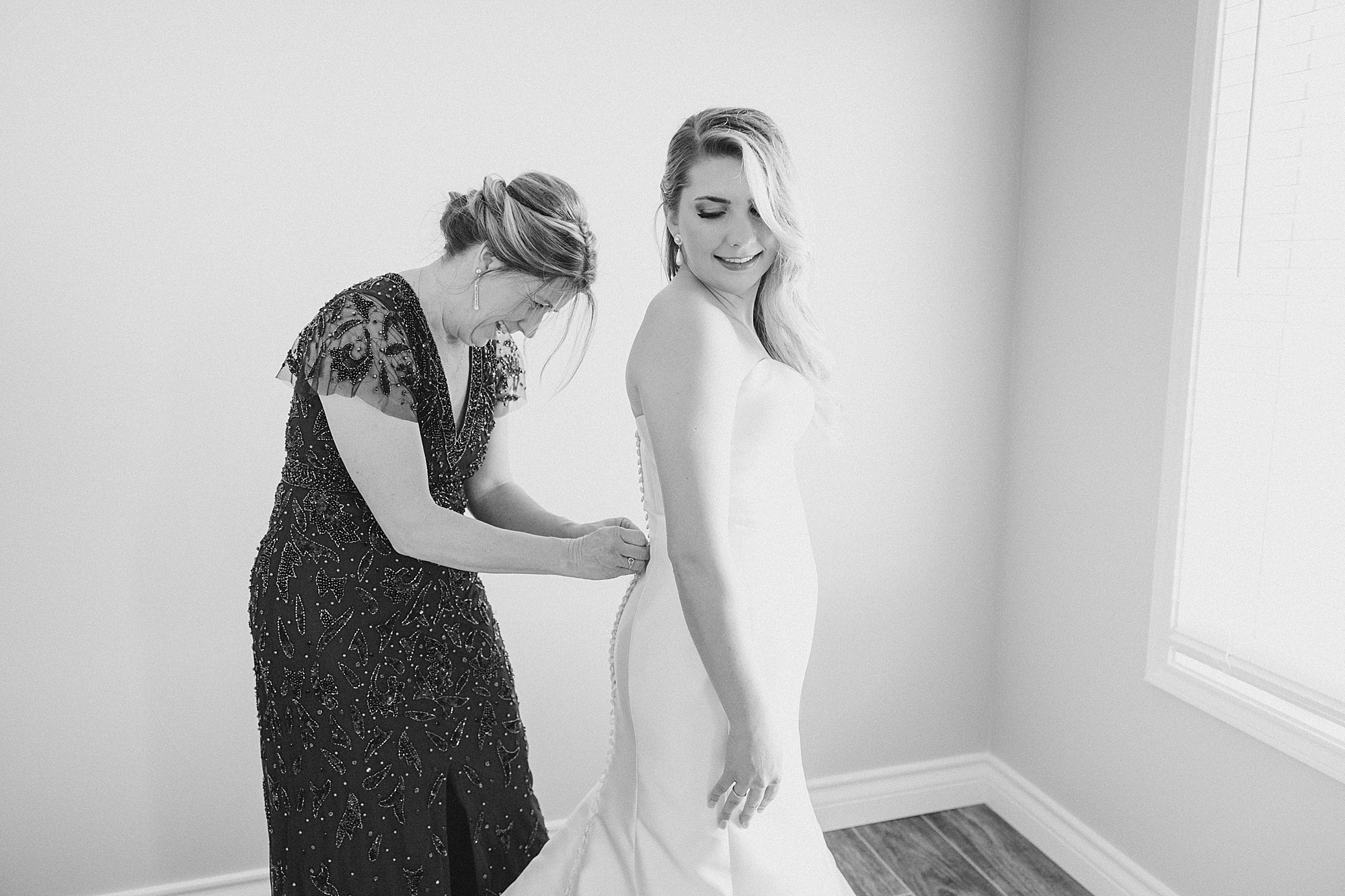 mother helps bride with wedding dress
