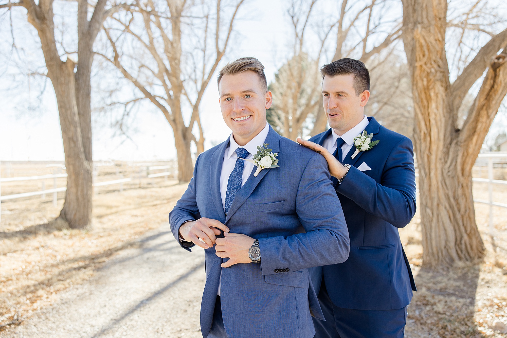 groomsman helps groom with navy suit jacket