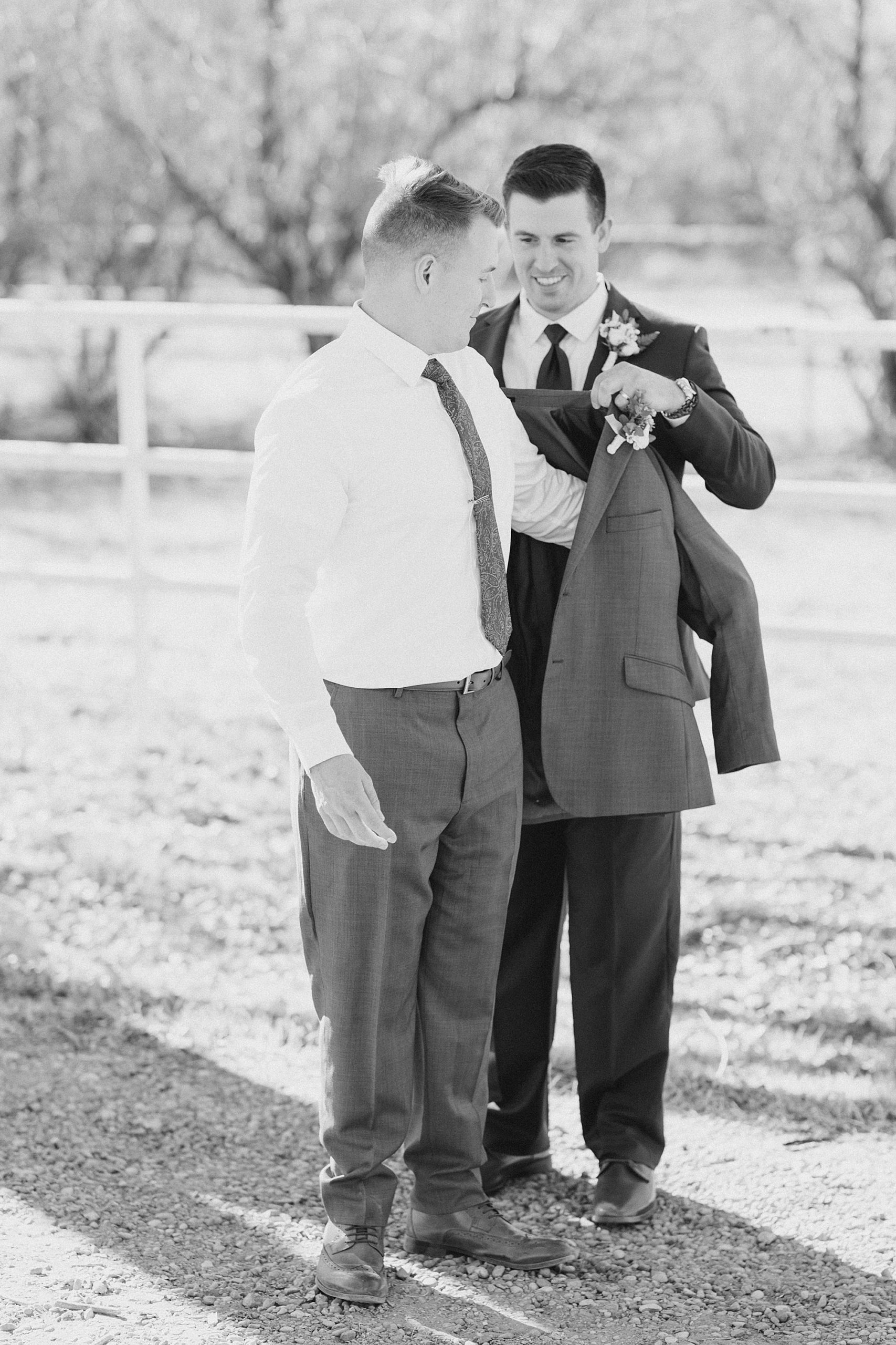 groomsman helps groom into jacket before winter wedding day