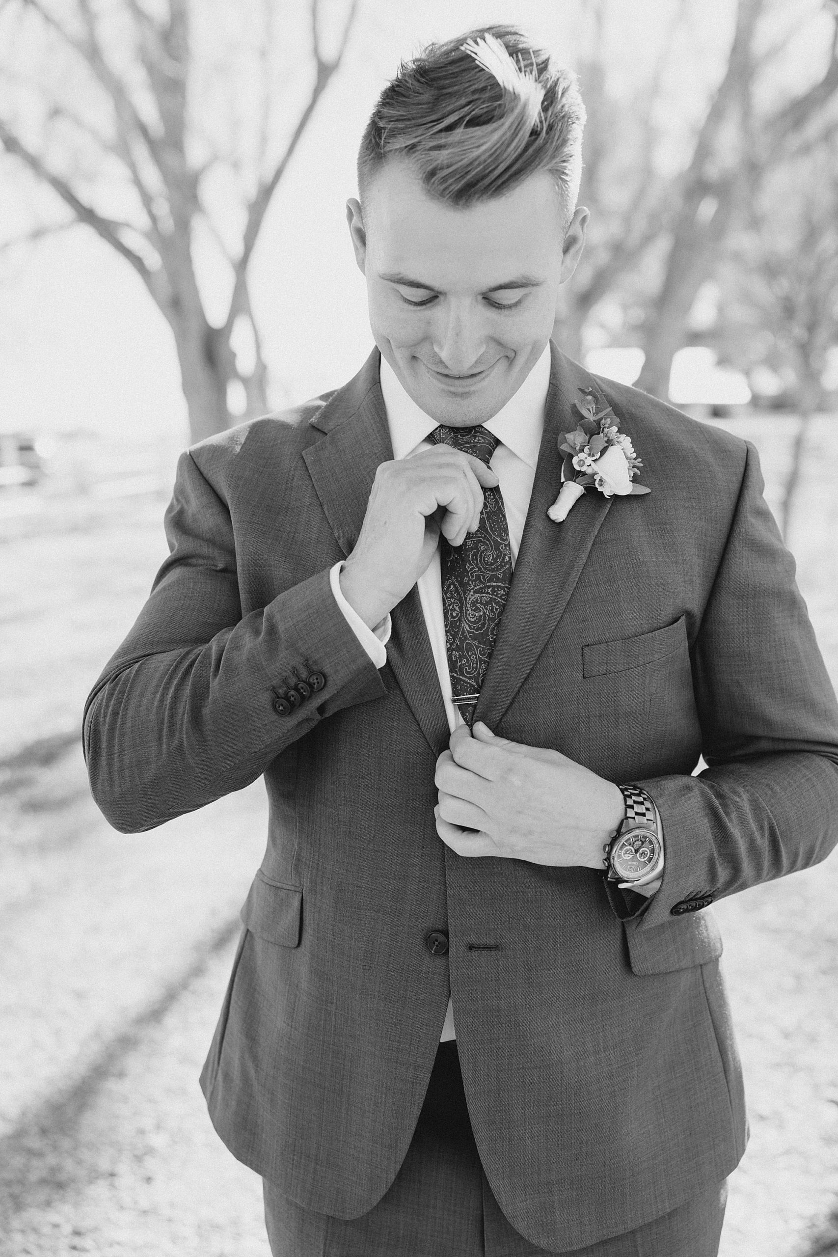 groom adjusts tie while preparing for winter wedding