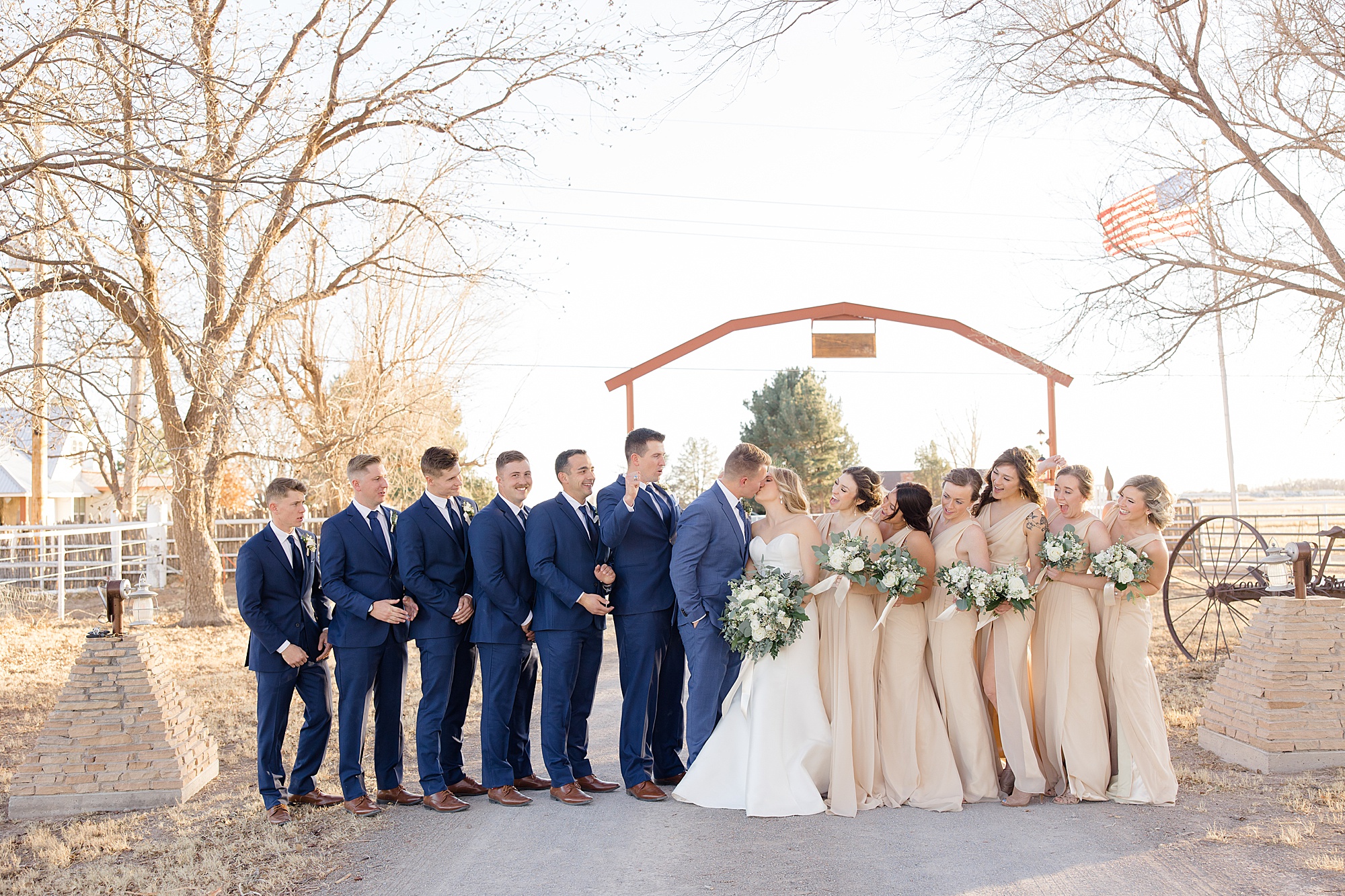 bride and groom kiss with wedding party around them on family farm