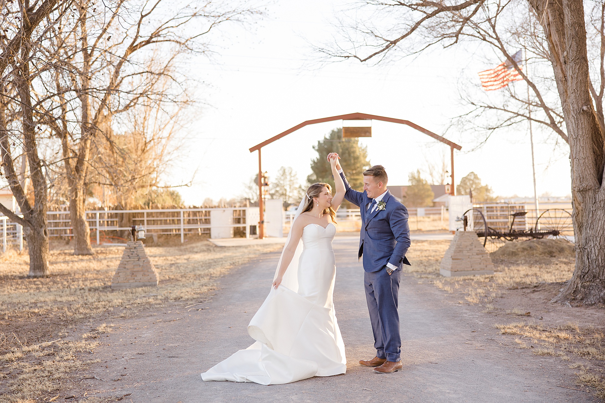 groom twirls bride under wooden sign on family farm