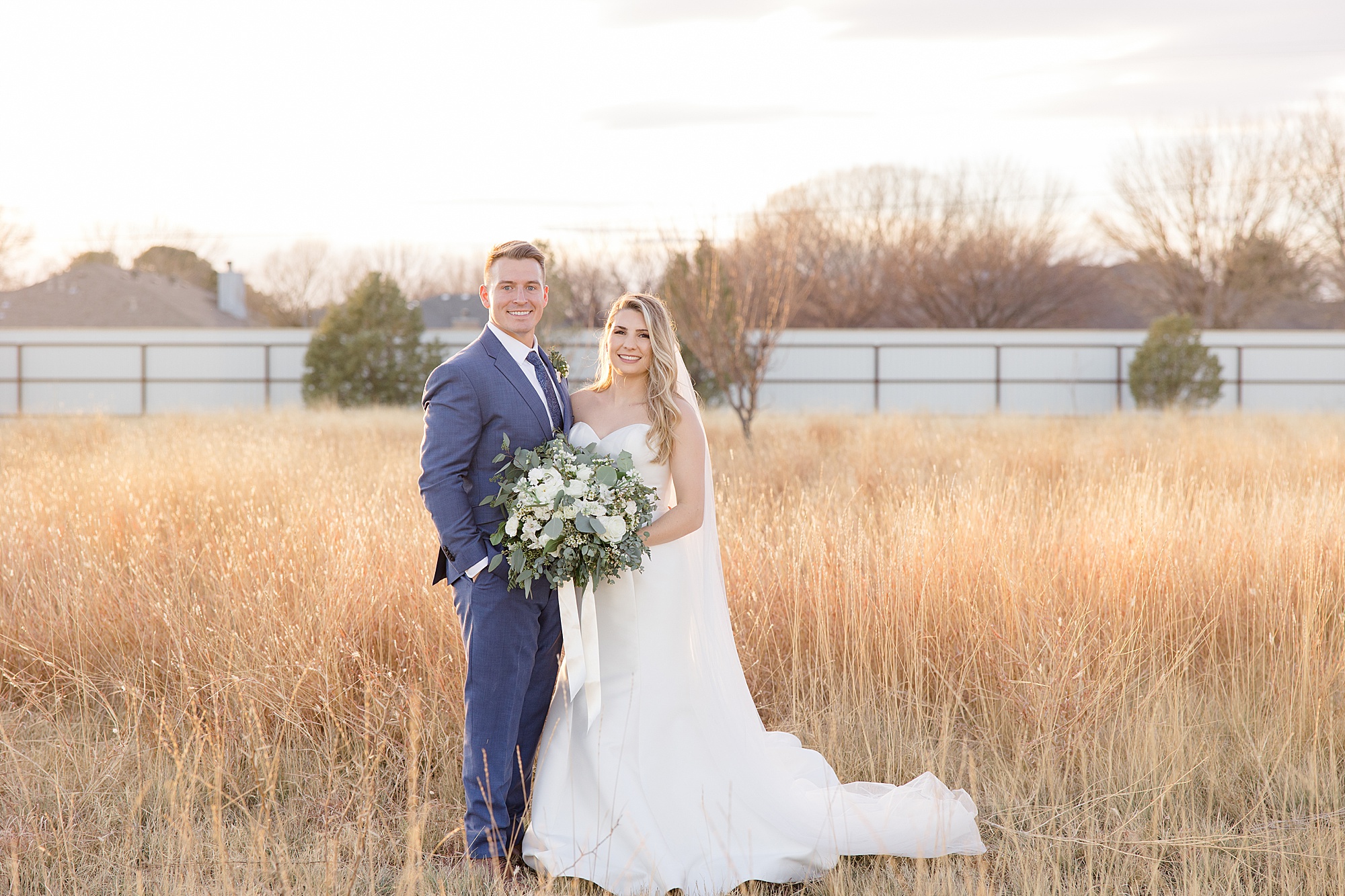 bride and groom stand in field at sunset