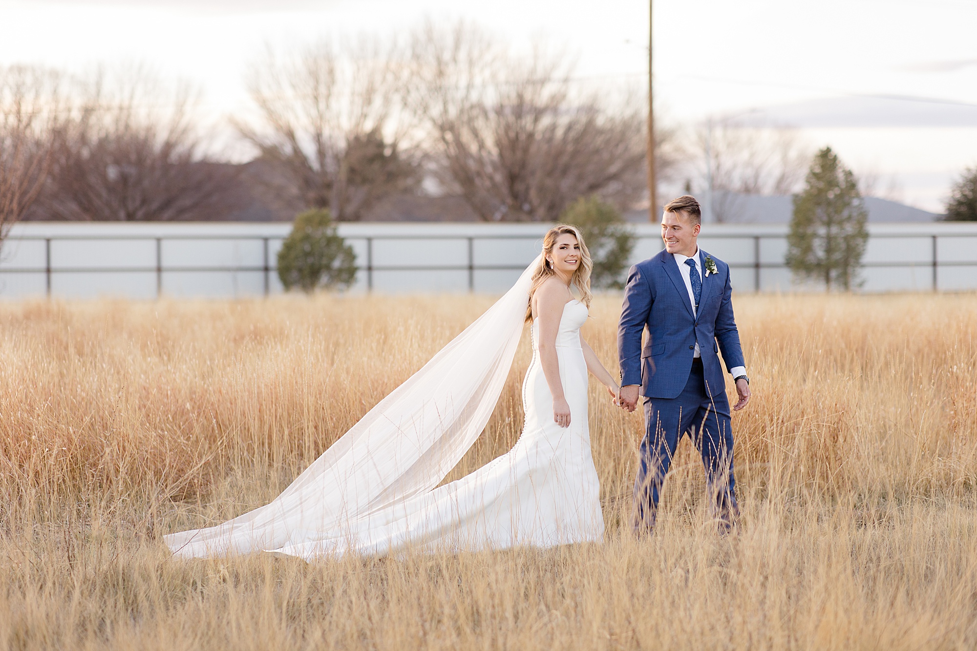 newlyweds walk together through field at sunset