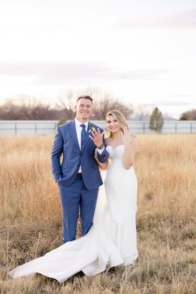 newlyweds show off wedding bands during portraits in field at sunset 