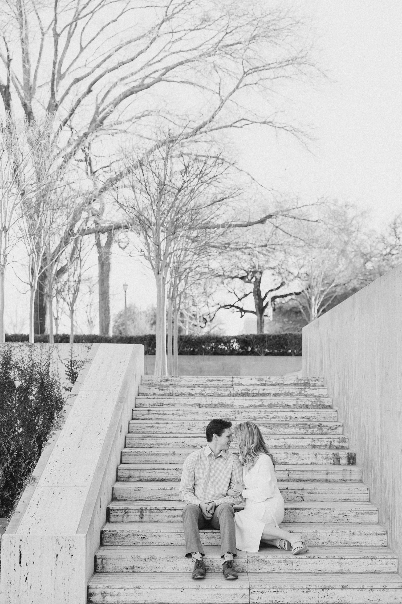 engaged couple kisses on steps in Texas museum gardens