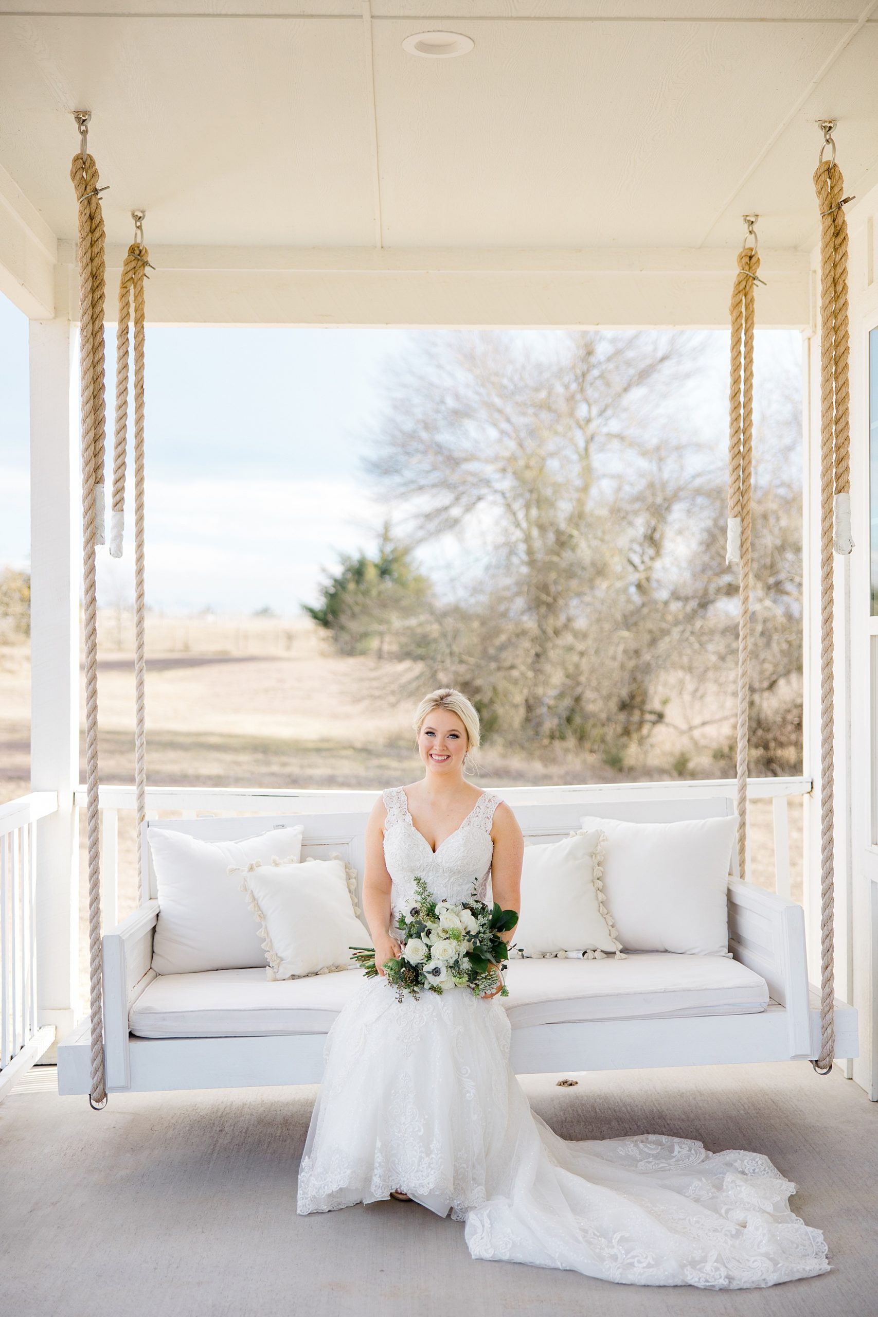bride sits on wooden swing with white pillows at The Grand Ivory