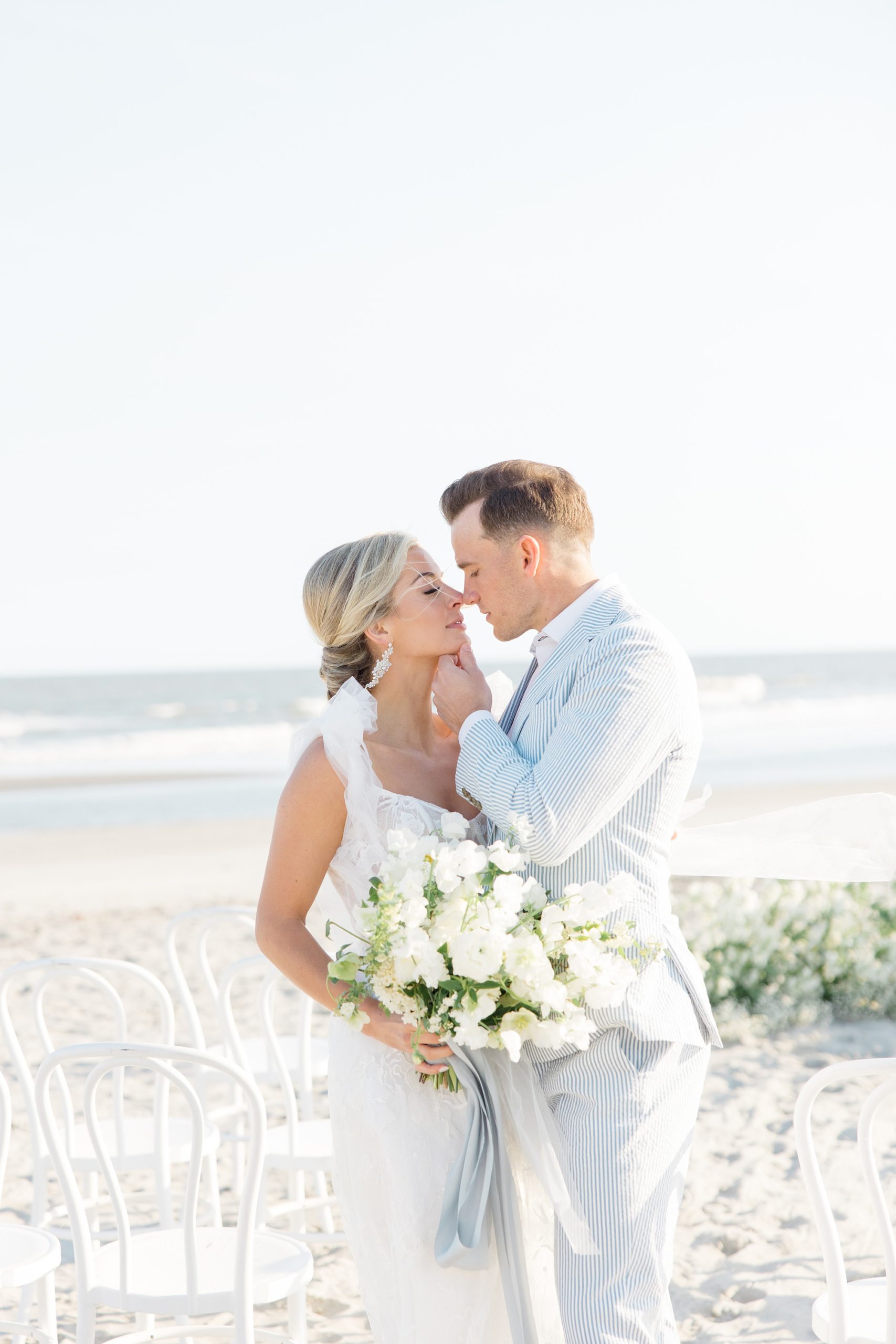 bride and groom stand together on Folly Beach with groom holding bride's chin
