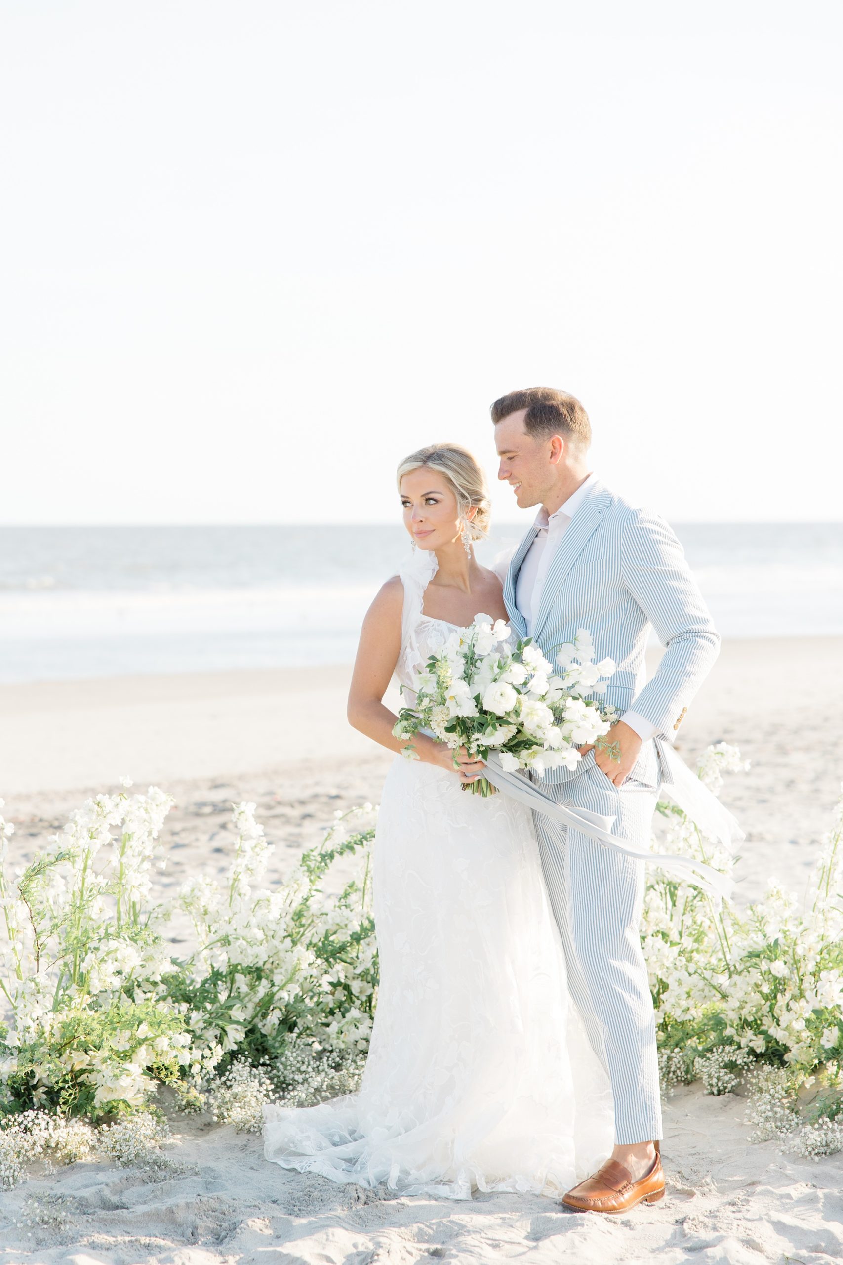 bride and grooms stand together by white floral installation at Folly Beach