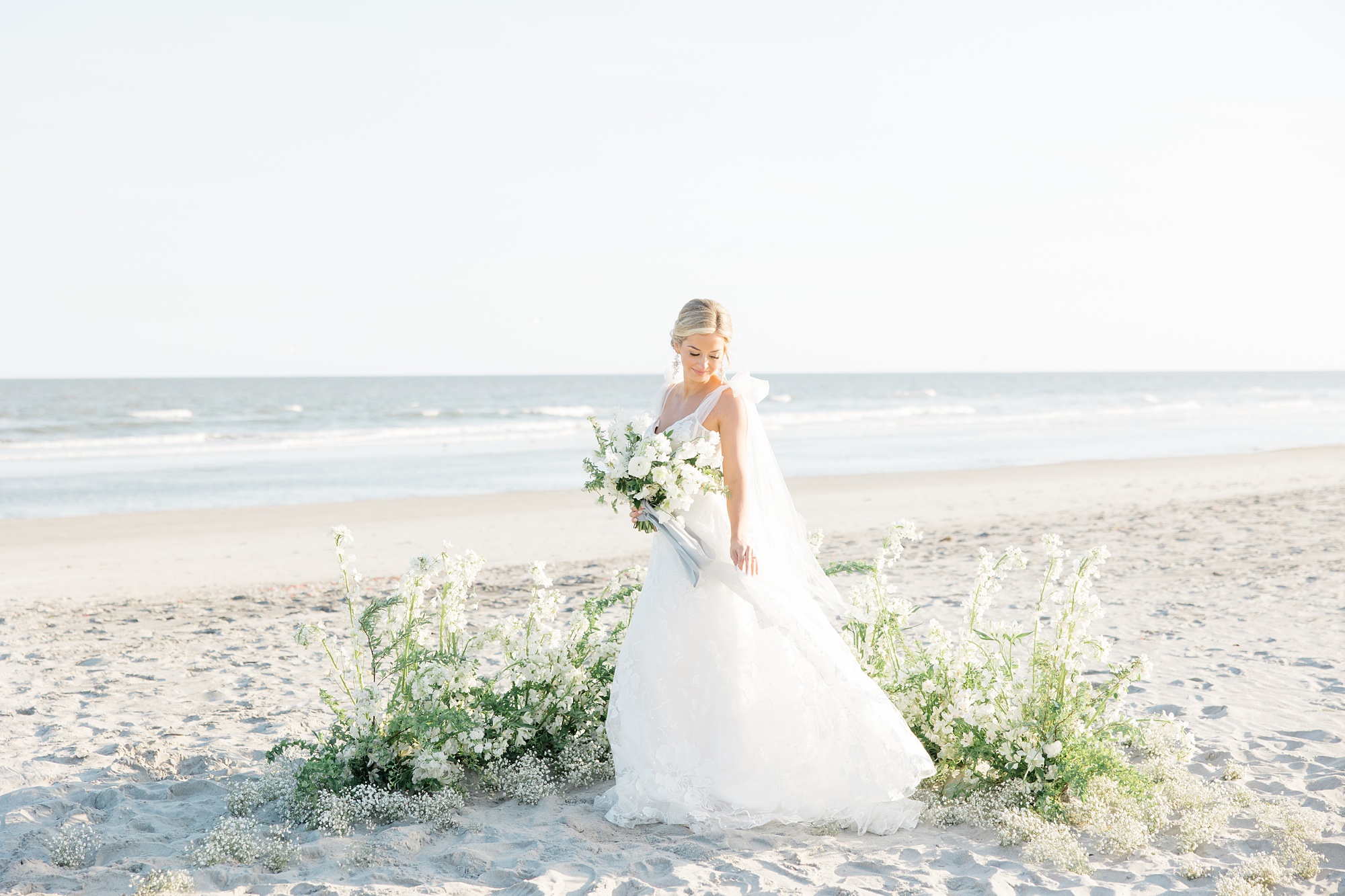 bride stands on beach by installation of white flowers on Folly Beach