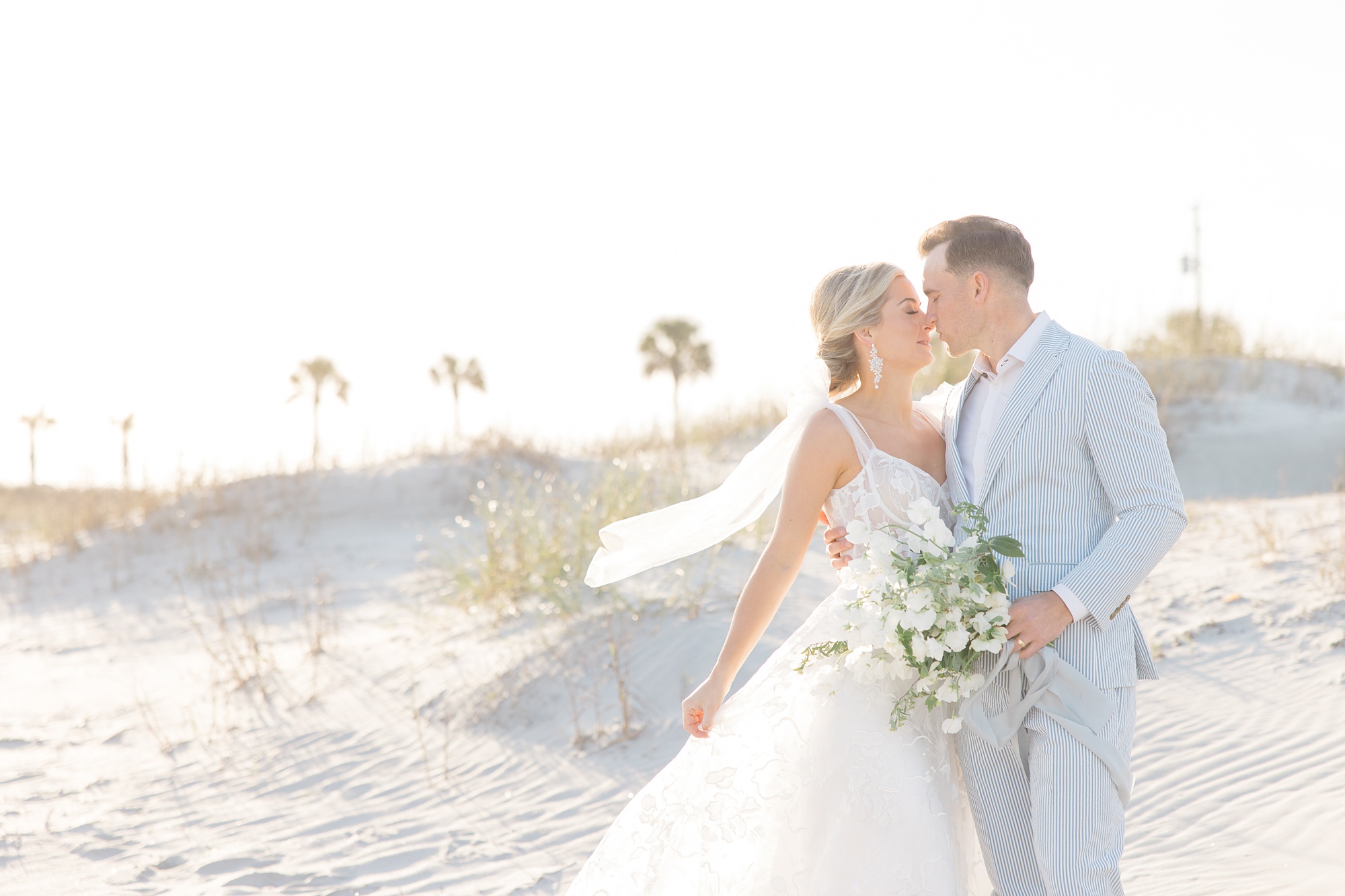 bride and groom kiss with bride's veil floating during Folly Beach wedding day