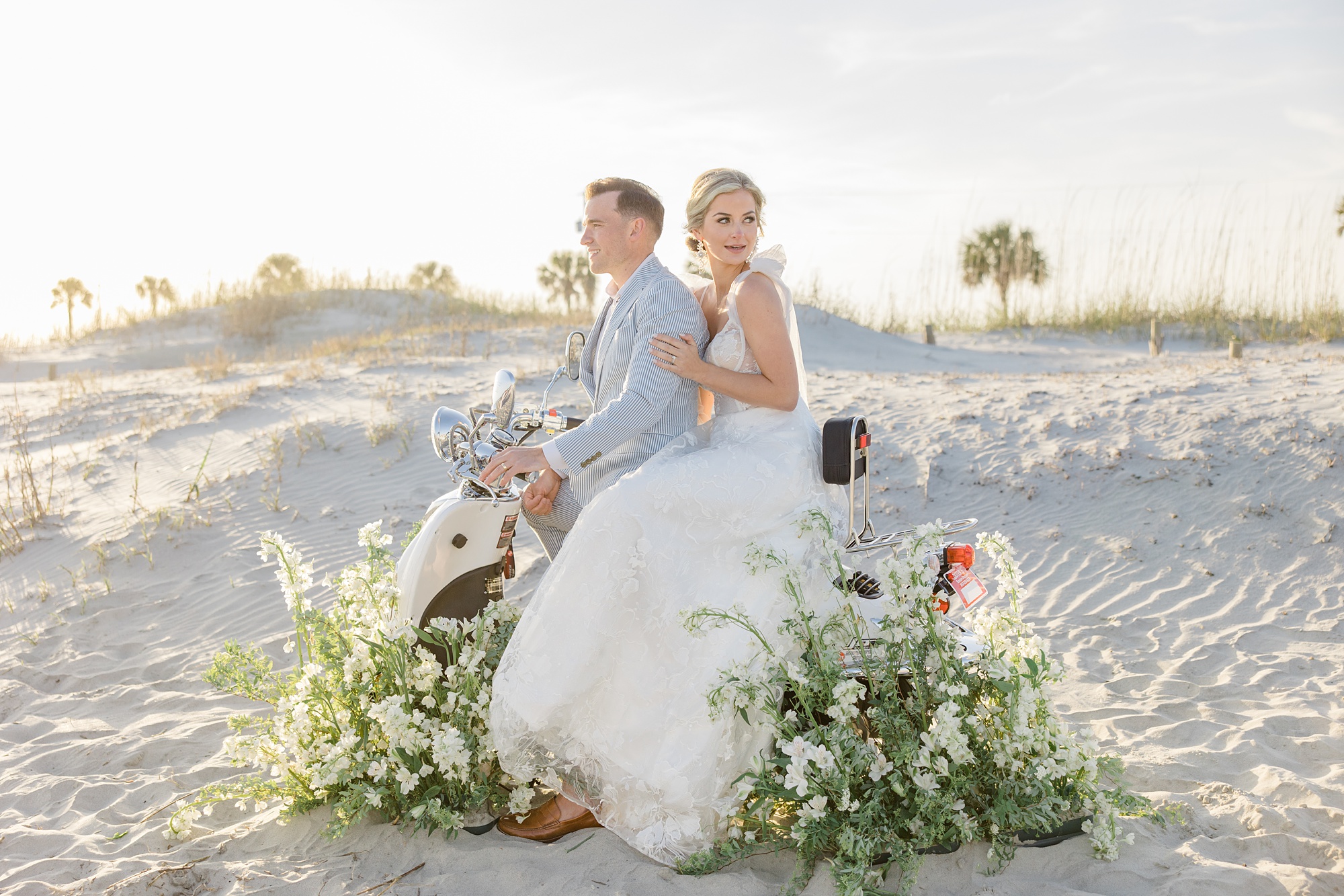newlyweds sit on white vespa with flowers around it on Folly Beach